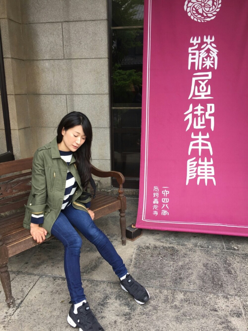 ブラック系のスニーカー、ブルー系のデニムパンツ、グリーン系のミリタリージャケットを着用したレディースの春コーディネートの1枚目の写真