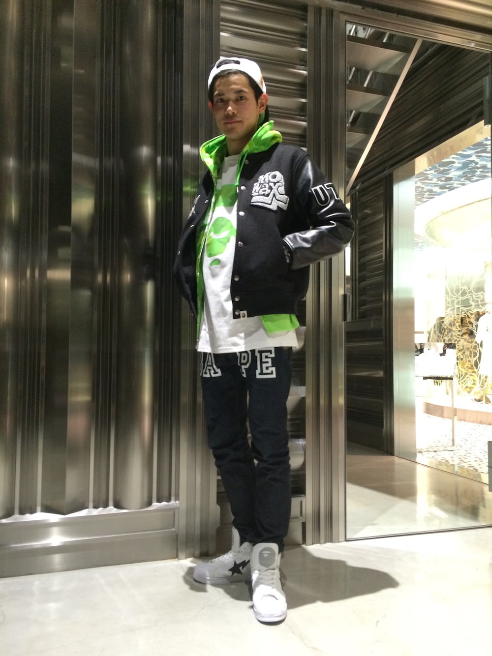 「スタジャン、カモフラ、Tシャツ、ジップパーカ、迷彩、オーバーサイズ、白スニーカー、総柄トップス、スナップバック、キャップ後ろかぶり」｜「A BATHING APEのMo' Wax VARSITY JACKET（スタジャン、ブラック系）」を使った、児玉 洋介さん（メンズ・176cm）の冬コーディネートの1枚目の写真