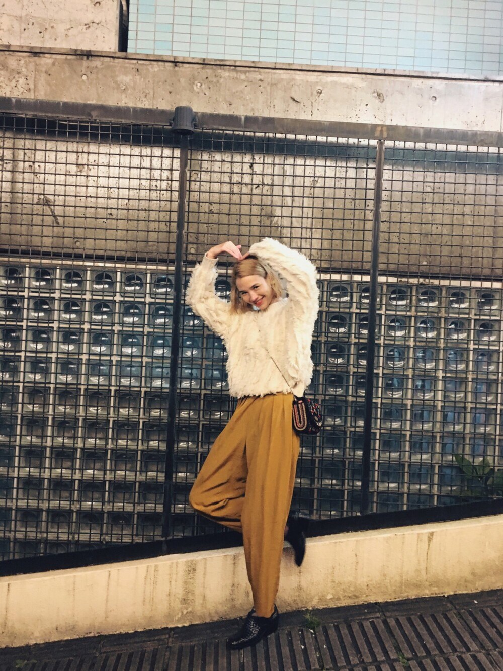 イエロー系のスラックス、ブラック系のブーツ、ホワイト系のニット/セーターを着用したレディースの秋コーディネートの1枚目の写真