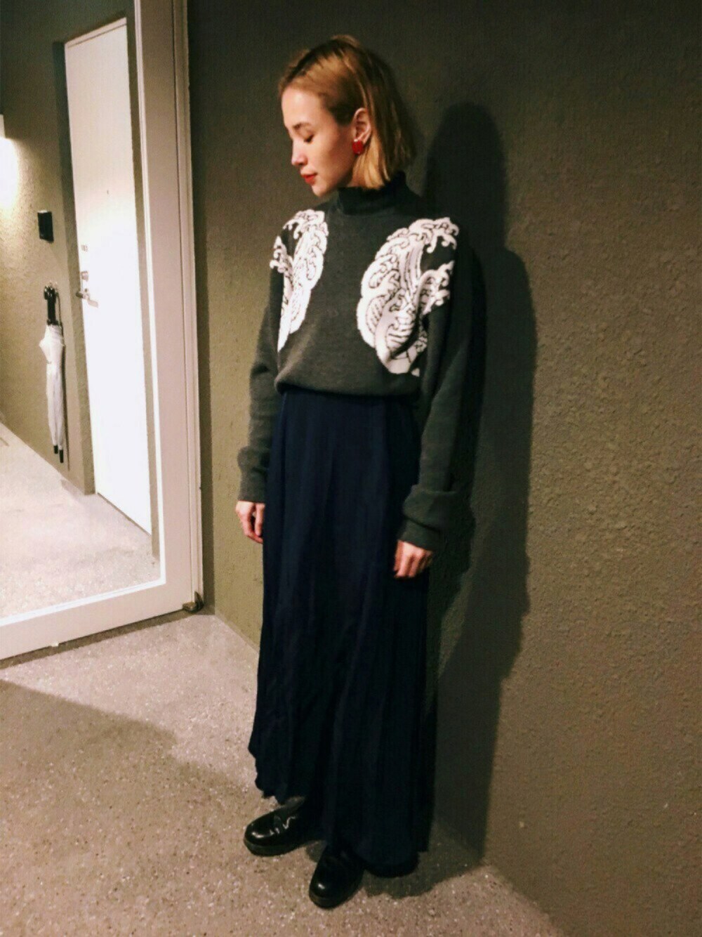 グレー系のニット/セーター、ブルー系のスカート、レッド系のピアス(両耳用)を着用したレディースの冬コーディネートの1枚目の写真