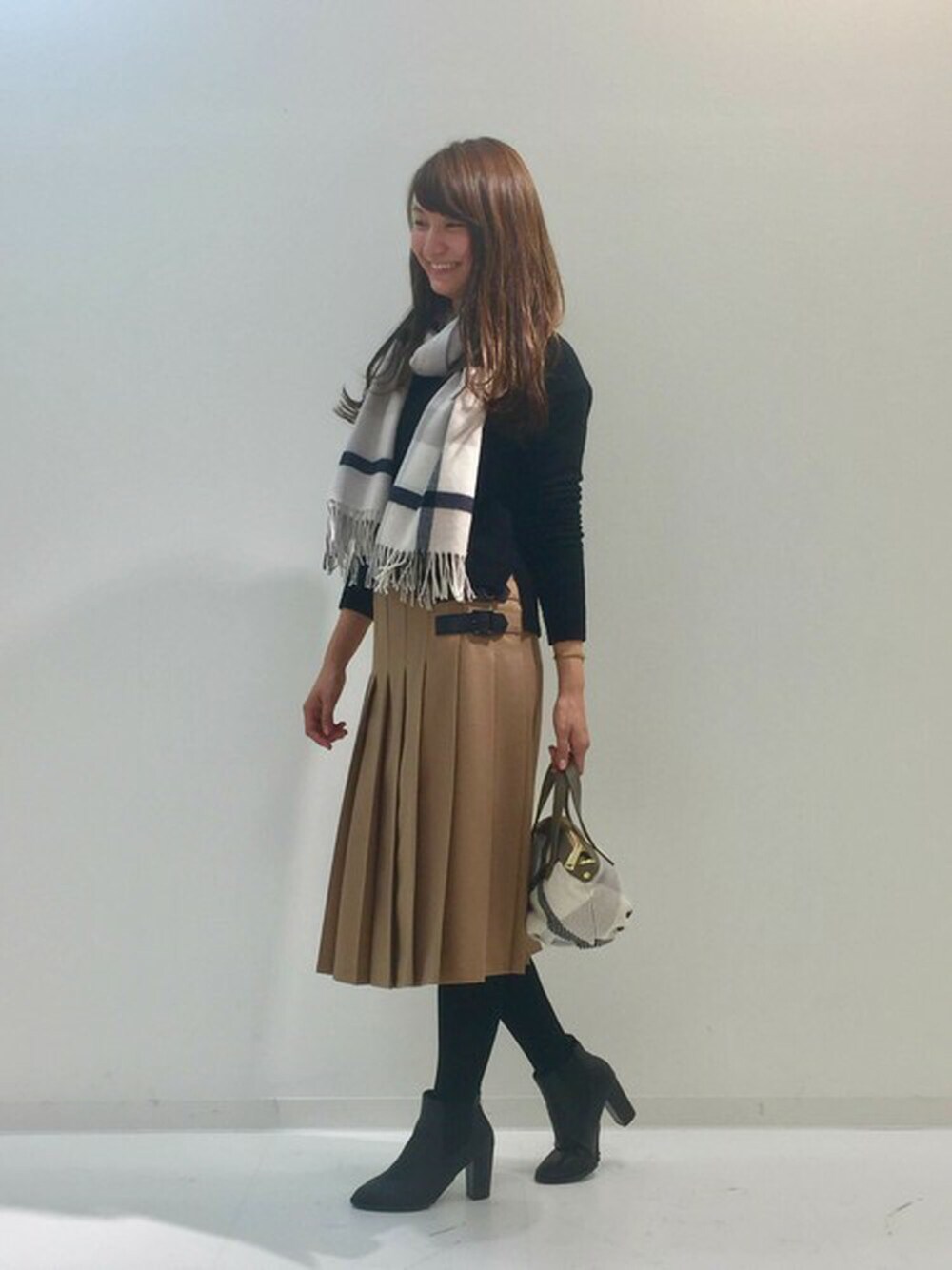 ブラック系のニット/セーター、ベージュ系のスカート、ホワイト系のショルダーバッグを着用したレディースの冬コーディネートの1枚目の写真