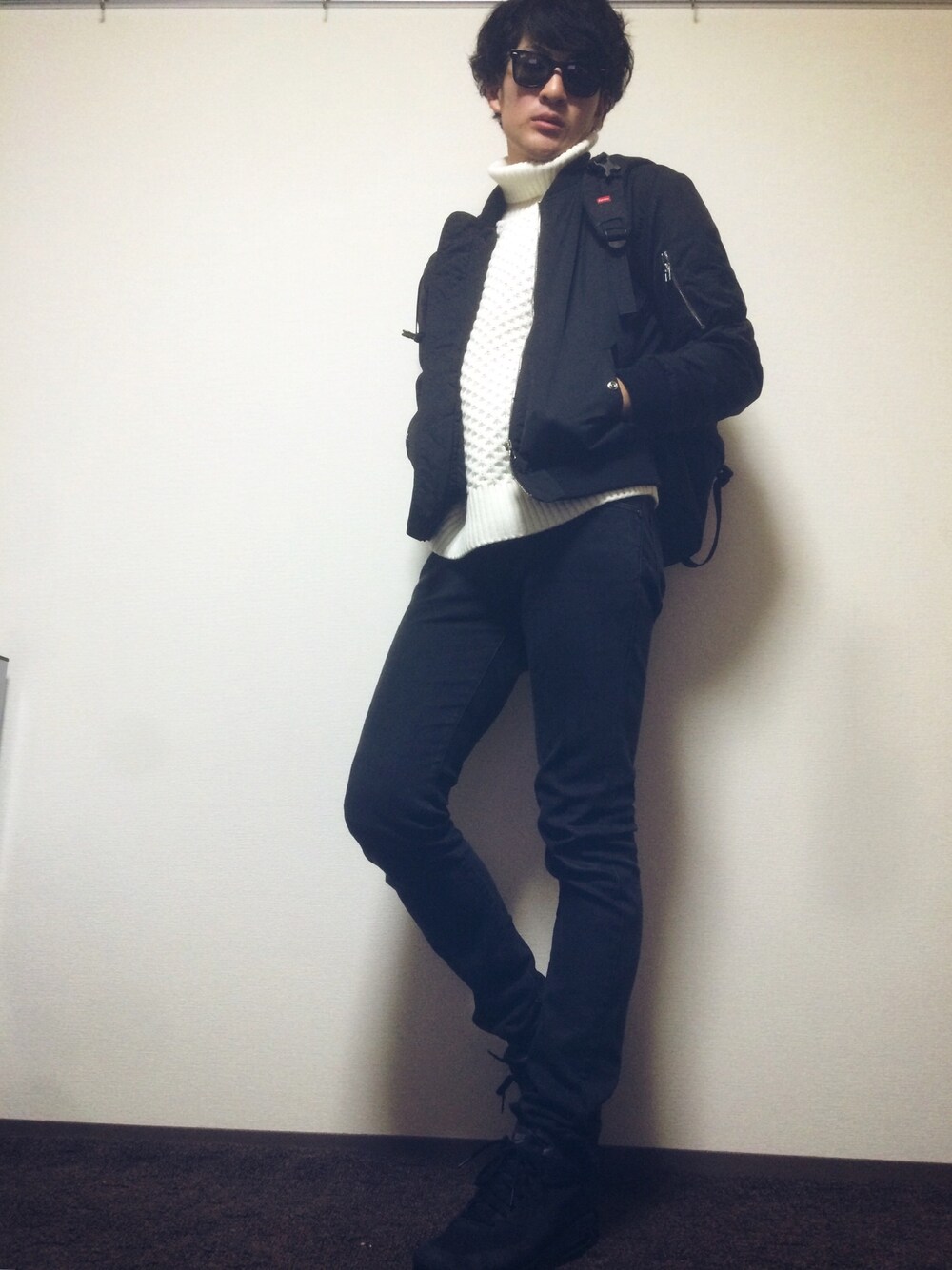 ブラック系のバックパック/リュック、ブラック系のミリタリージャケット、ホワイト系のニット/セーターを着用したメンズの冬コーディネートの1枚目の写真