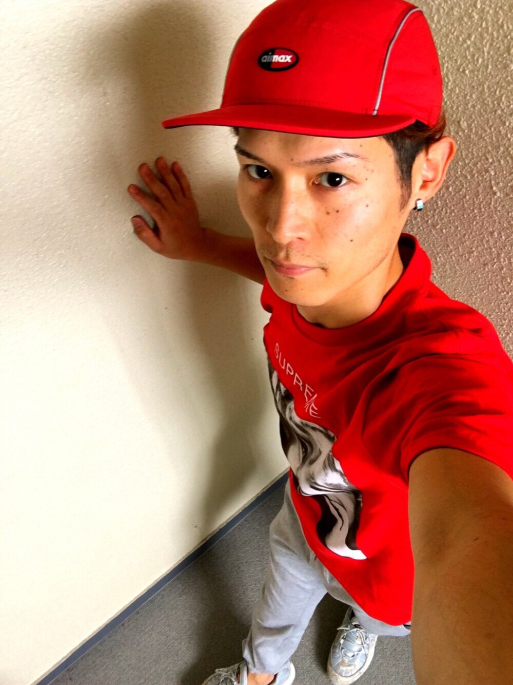 グレー系のパンツ、レッド系のTシャツ/カットソー、グレー系のスニーカーを着用したメンズの夏コーディネートの1枚目の写真