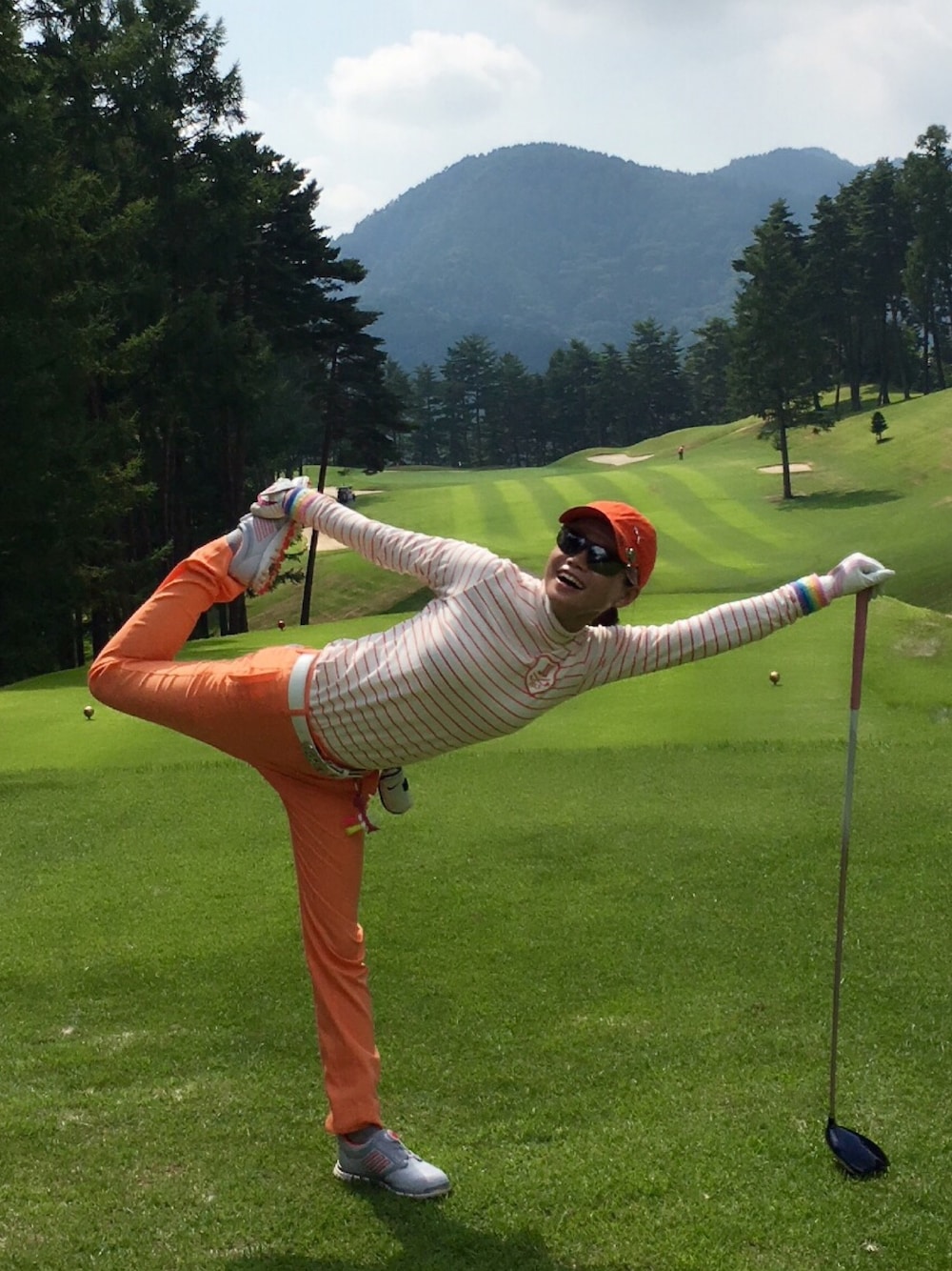 オレンジ系のその他パンツ、オレンジ系のポロシャツ、グレー系のゴルフグッズを着用したレディースの秋コーディネートの1枚目の写真