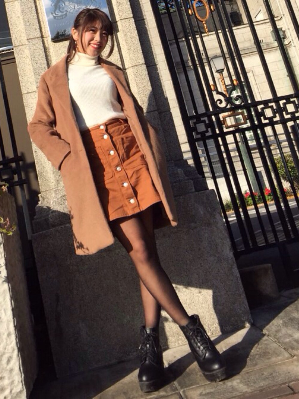 ベージュ系のチェスターコート、ホワイト系のニット/セーター、ブラウン系のデニムスカートを着用したレディースの冬コーディネートの1枚目の写真