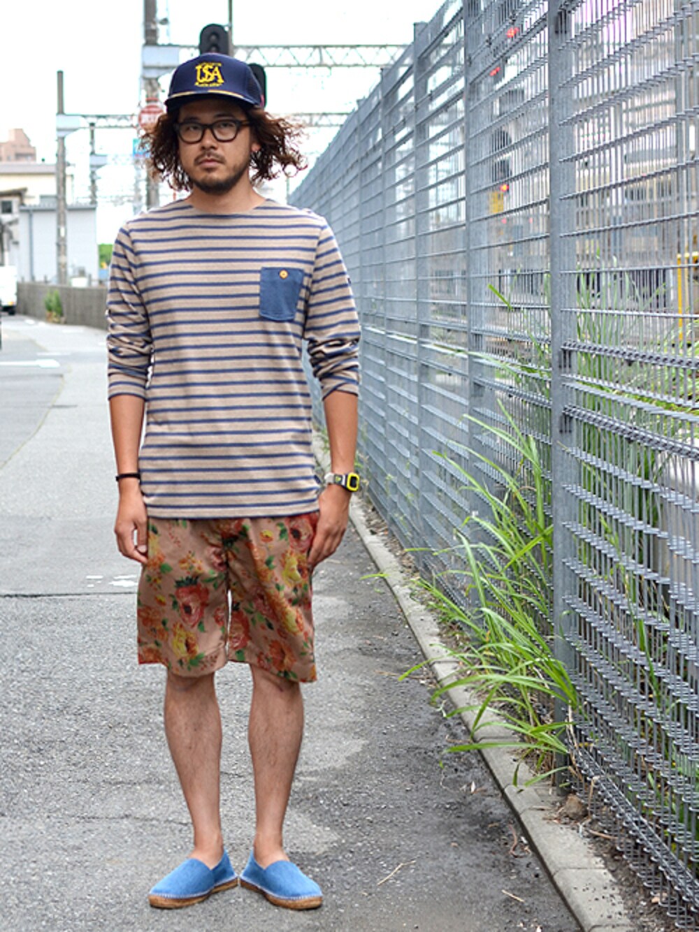 ベージュ系のスラックス、ブルー系のキャップを着用したメンズの夏コーディネートの1枚目の写真