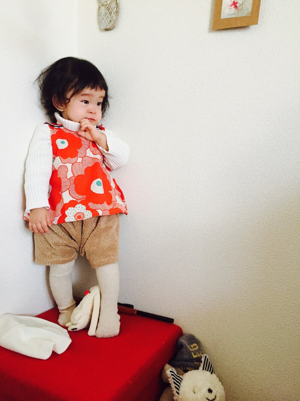 レッド系のチュニック、ホワイト系のニット/セーター、ベージュ系のパンツを着用したキッズの秋コーディネートの1枚目の写真