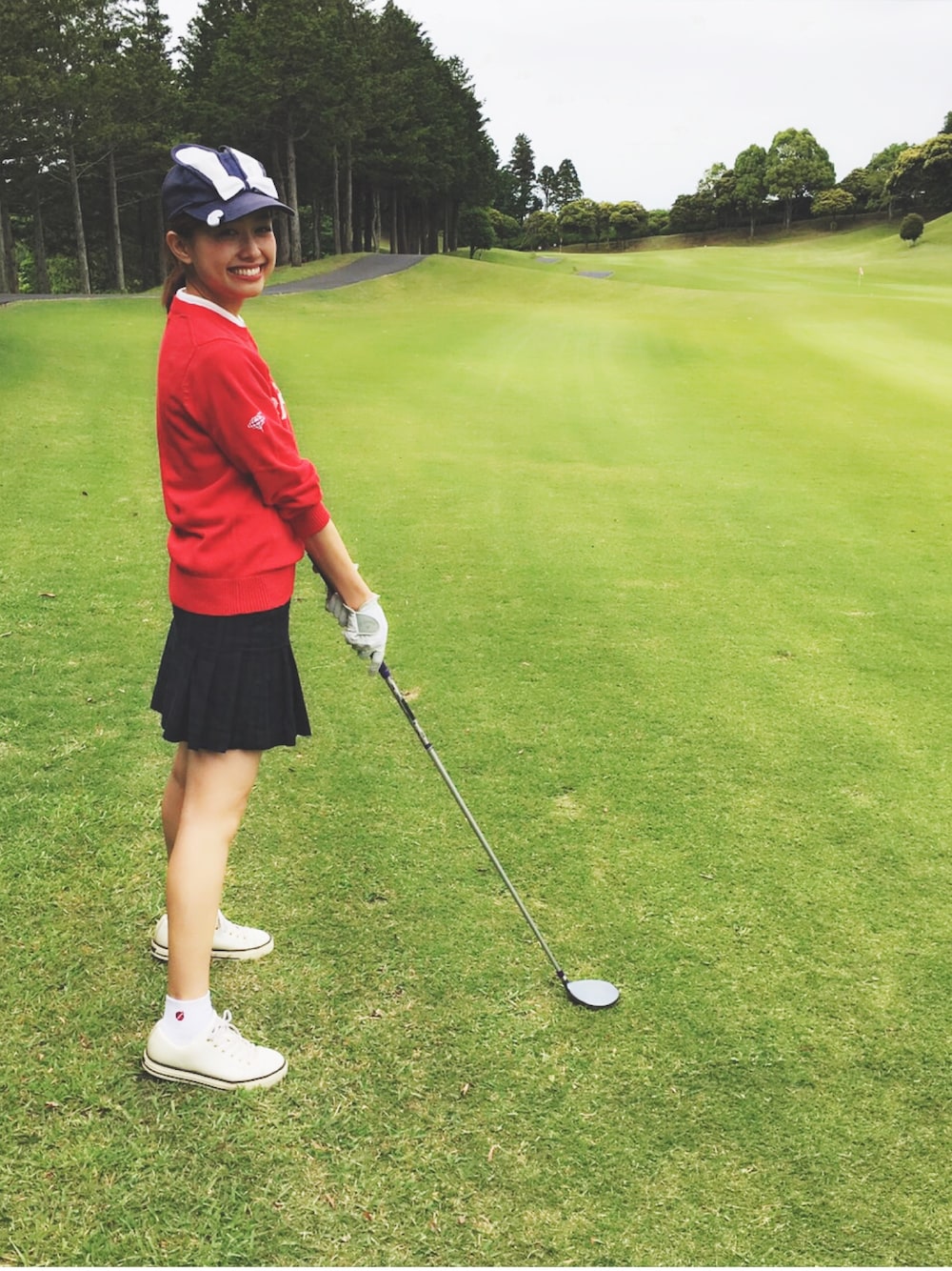 ホワイト系のポロシャツ、レッド系のニット/セーター、グリーン系のスカートを着用したレディースの春コーディネートの1枚目の写真