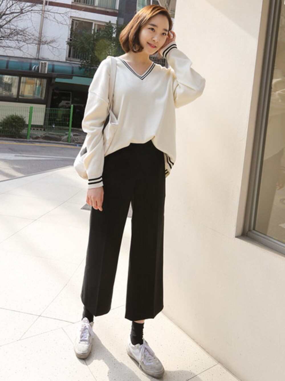 ホワイト系のニット/セーター、ブラック系のスラックスを着用したレディースの春コーディネートの1枚目の写真