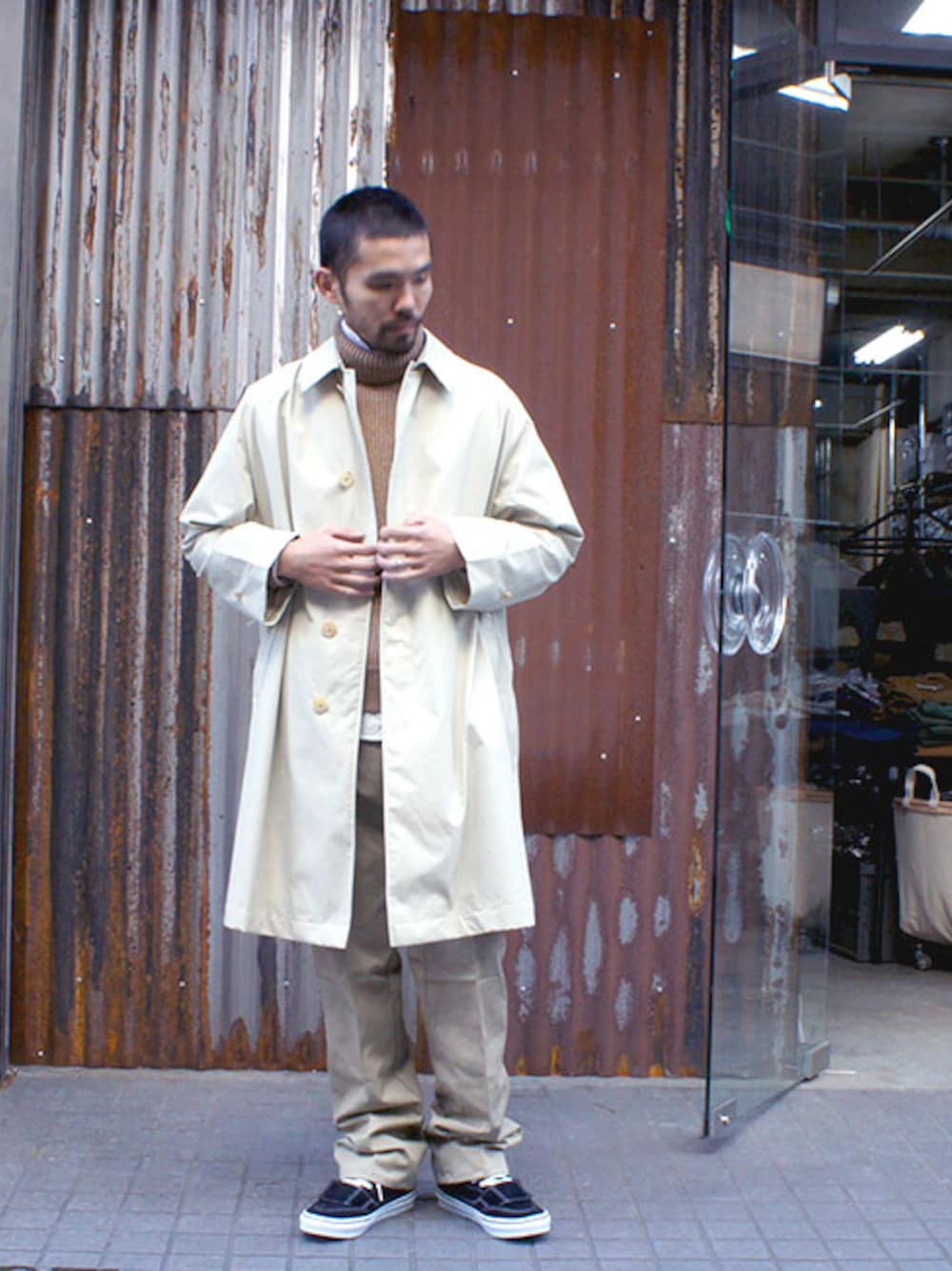 ベージュ系のステンカラーコート、ブラウン系のニット/セーター、ホワイト系のシャツ/ブラウスを着用したメンズの秋コーディネートの1枚目の写真