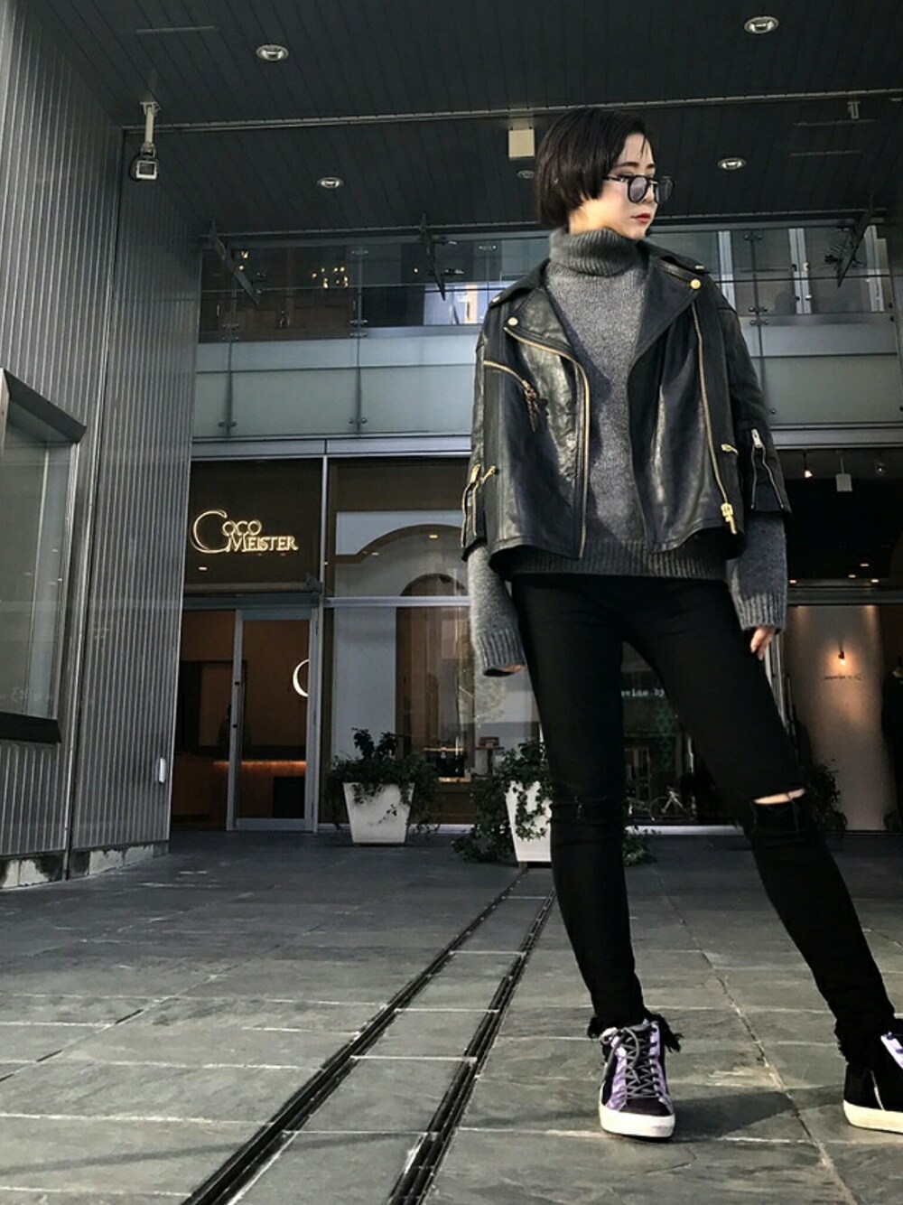 ブラック系のライダースジャケット、パープル系のスニーカー、ブラック系のサングラスを着用したレディースの秋コーディネートの1枚目の写真