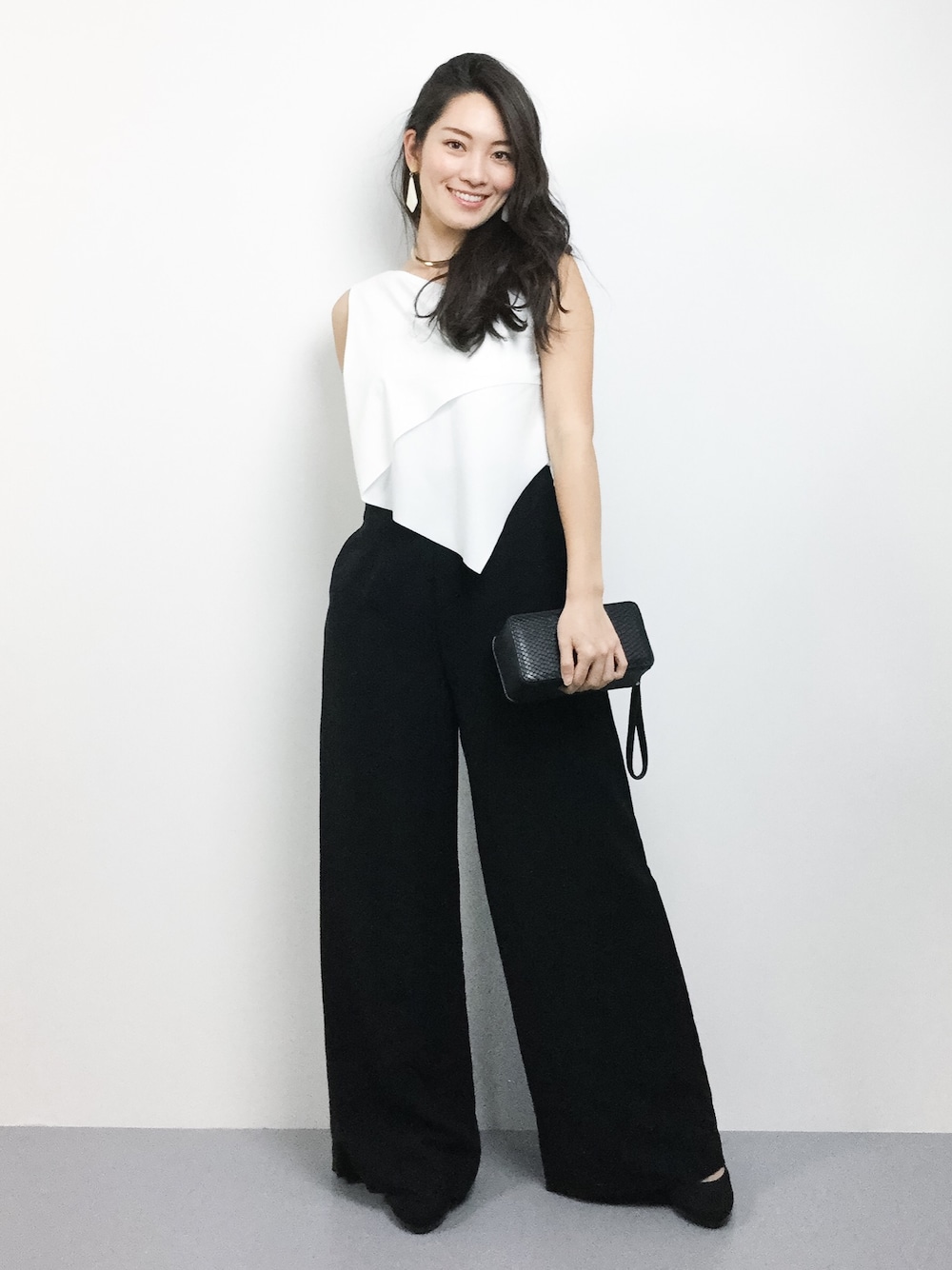 ホワイト系のパンツドレス、ブラック系のクラッチバッグを着用したレディースの秋コーディネートの1枚目の写真