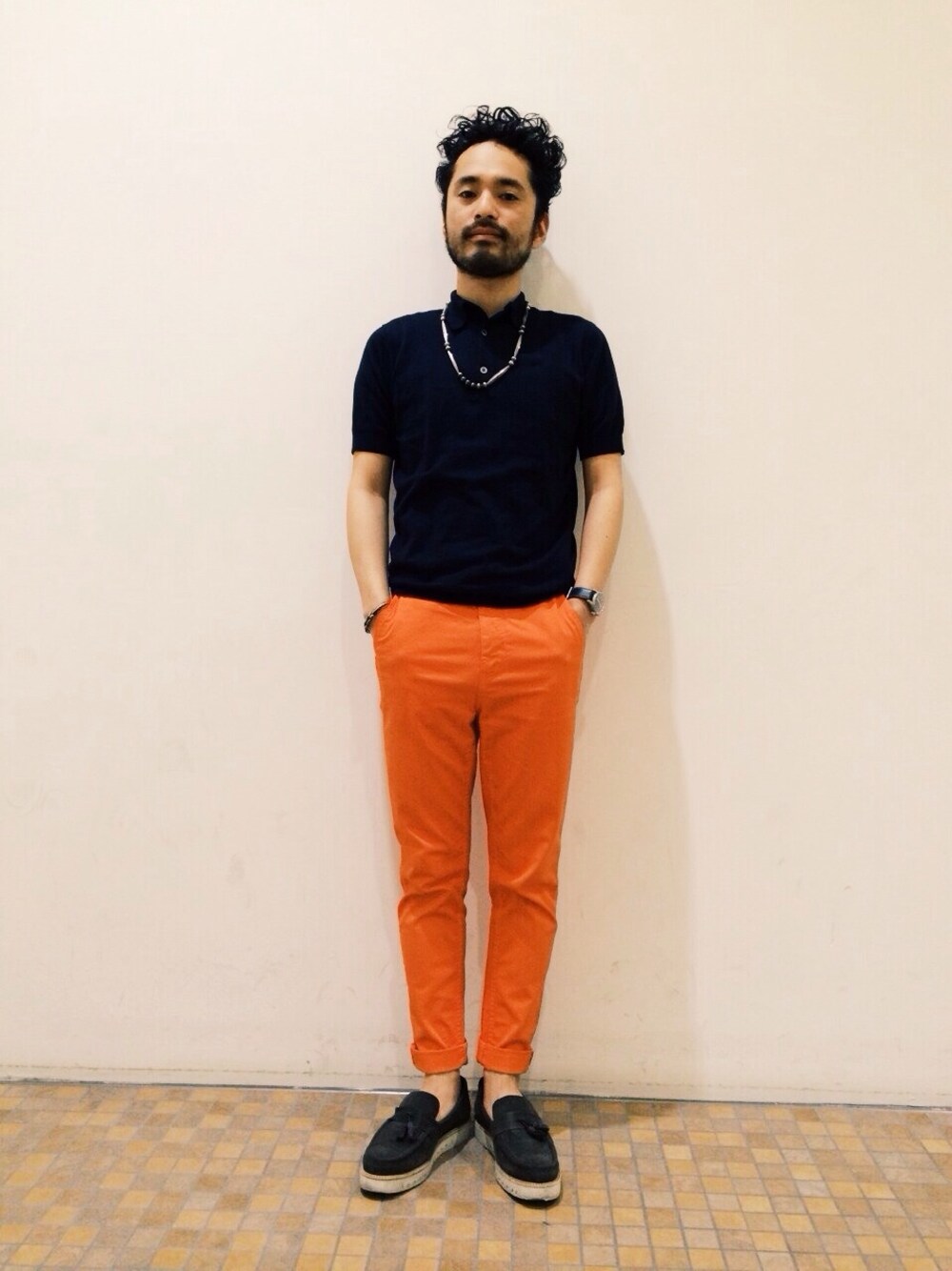 ブルー系のポロシャツ、オレンジ系のチノパンツ、グレー系のその他シューズを着用したメンズの春コーディネートの1枚目の写真