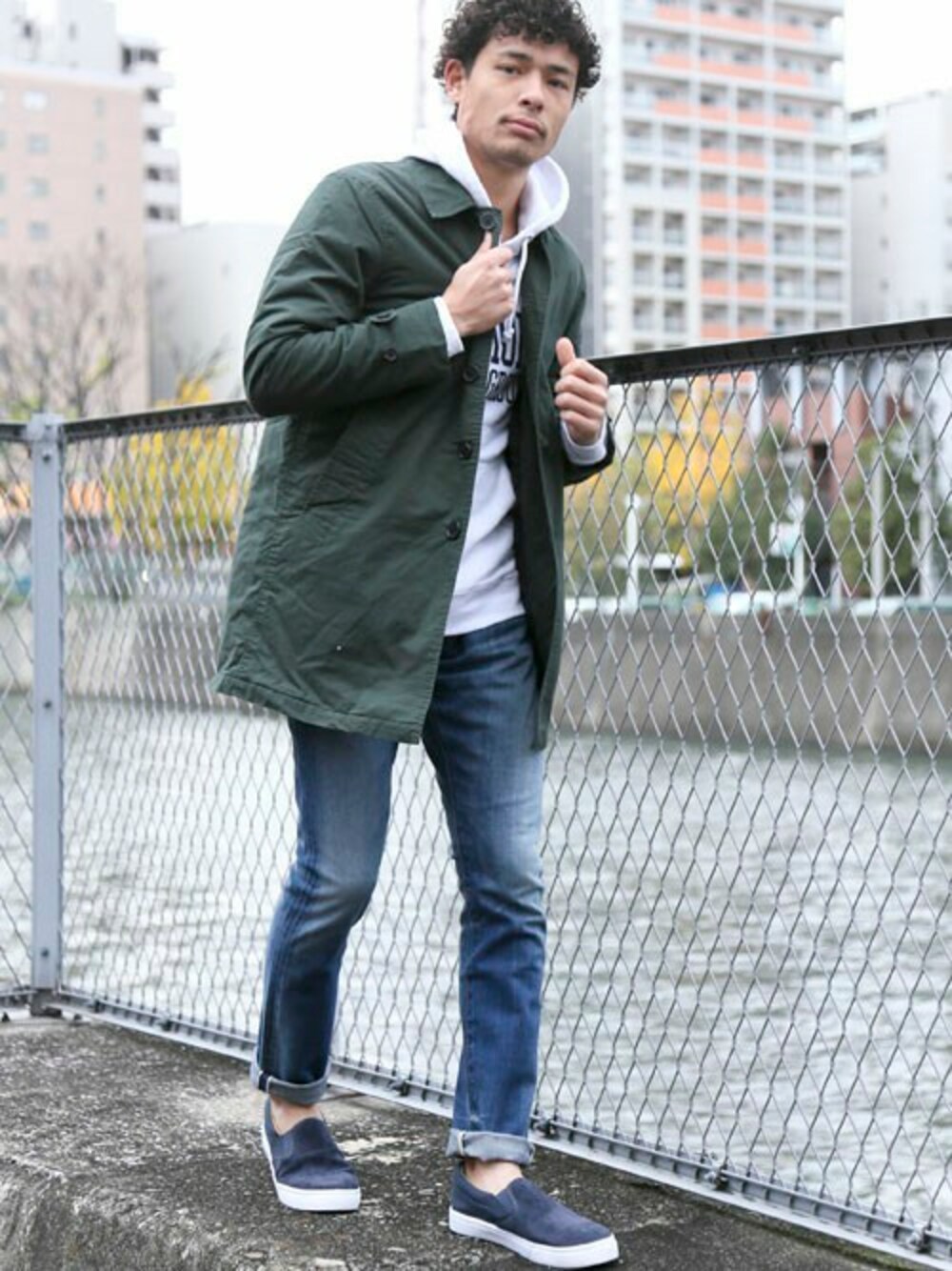ブルー系のデニムパンツ、ホワイト系のパーカー、グリーン系のステンカラーコートを着用したメンズの冬コーディネートの1枚目の写真