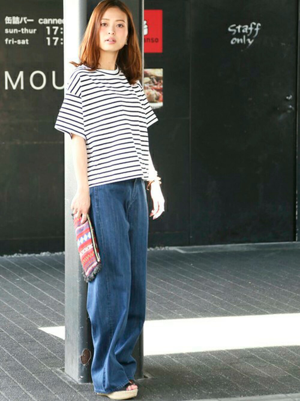 ブラック系のTシャツ/カットソー、ブルー系のデニムパンツ、レッド系のクラッチバッグを着用したレディースの春コーディネートの1枚目の写真