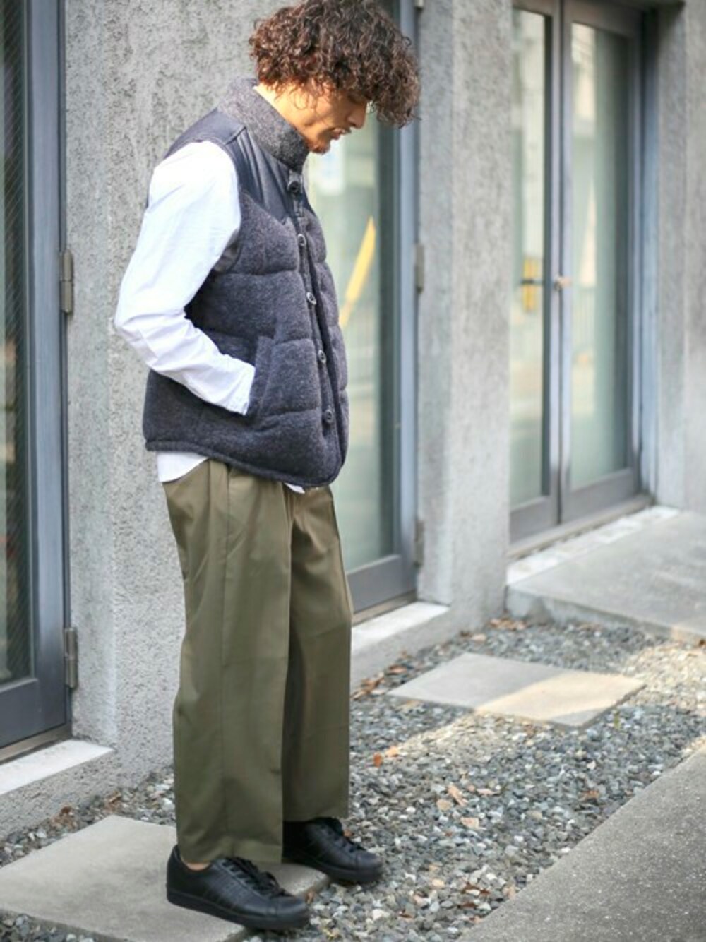グリーン系のチノパンツ、ブルー系のダウンベスト、ブラック系のスニーカーを着用したメンズの秋コーディネートの1枚目の写真