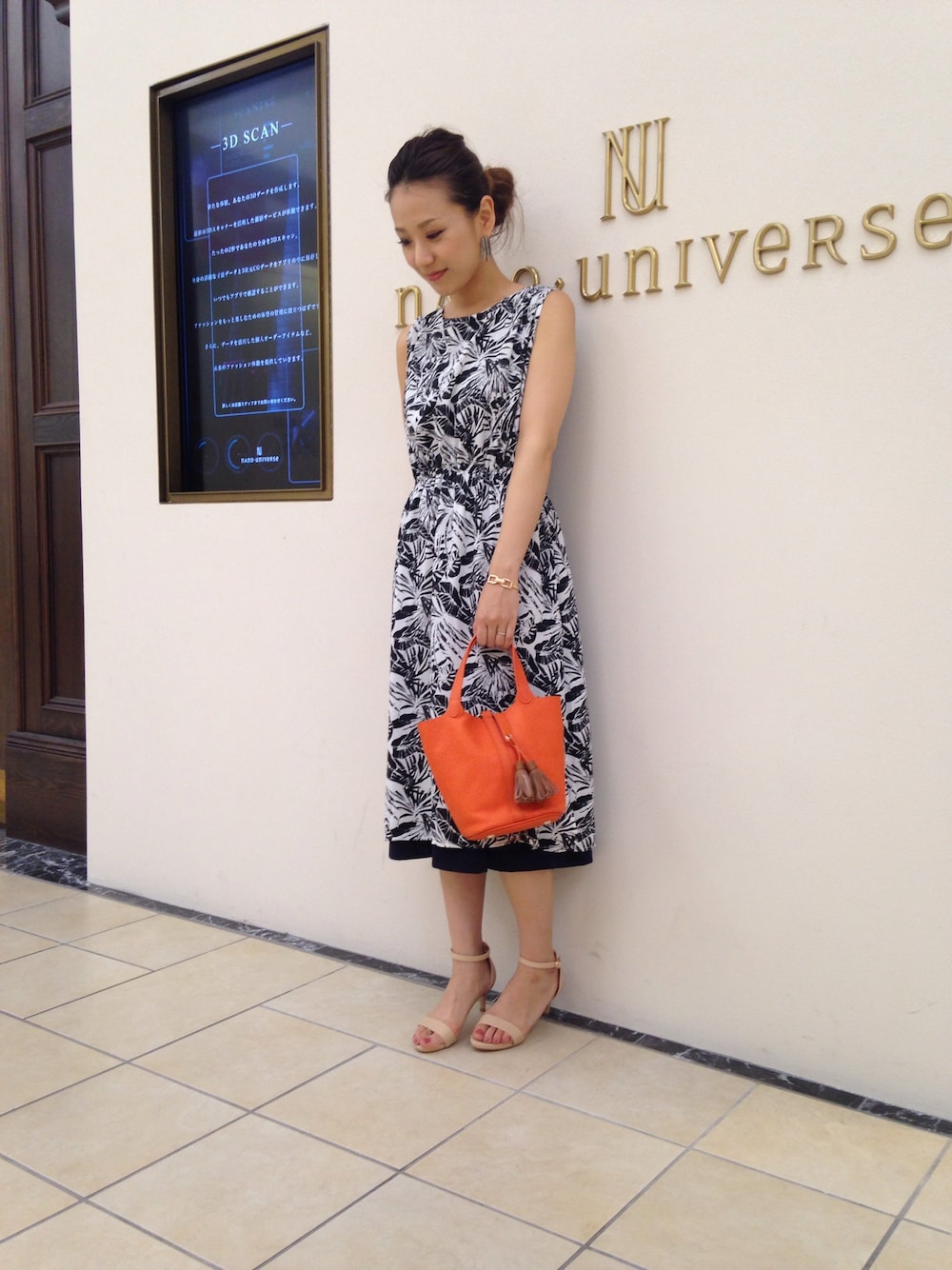 ブラック系のワンピース、オレンジ系のトートバッグ、ベージュ系のサンダルを着用したレディースの夏コーディネートの1枚目の写真