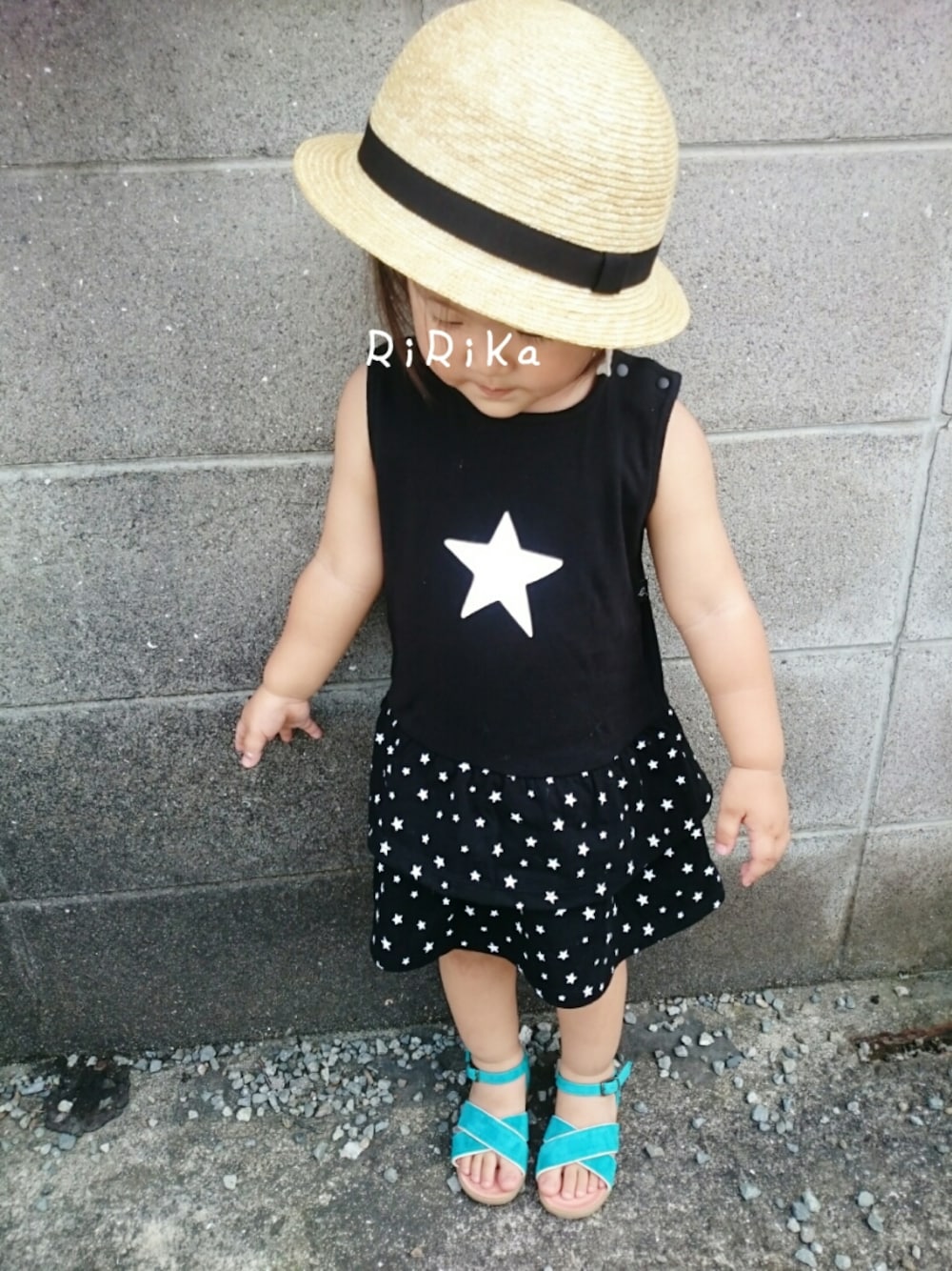 ブラック系のワンピース、ブルー系のサンダル、ベージュ系の帽子を着用したキッズの夏コーディネートの1枚目の写真