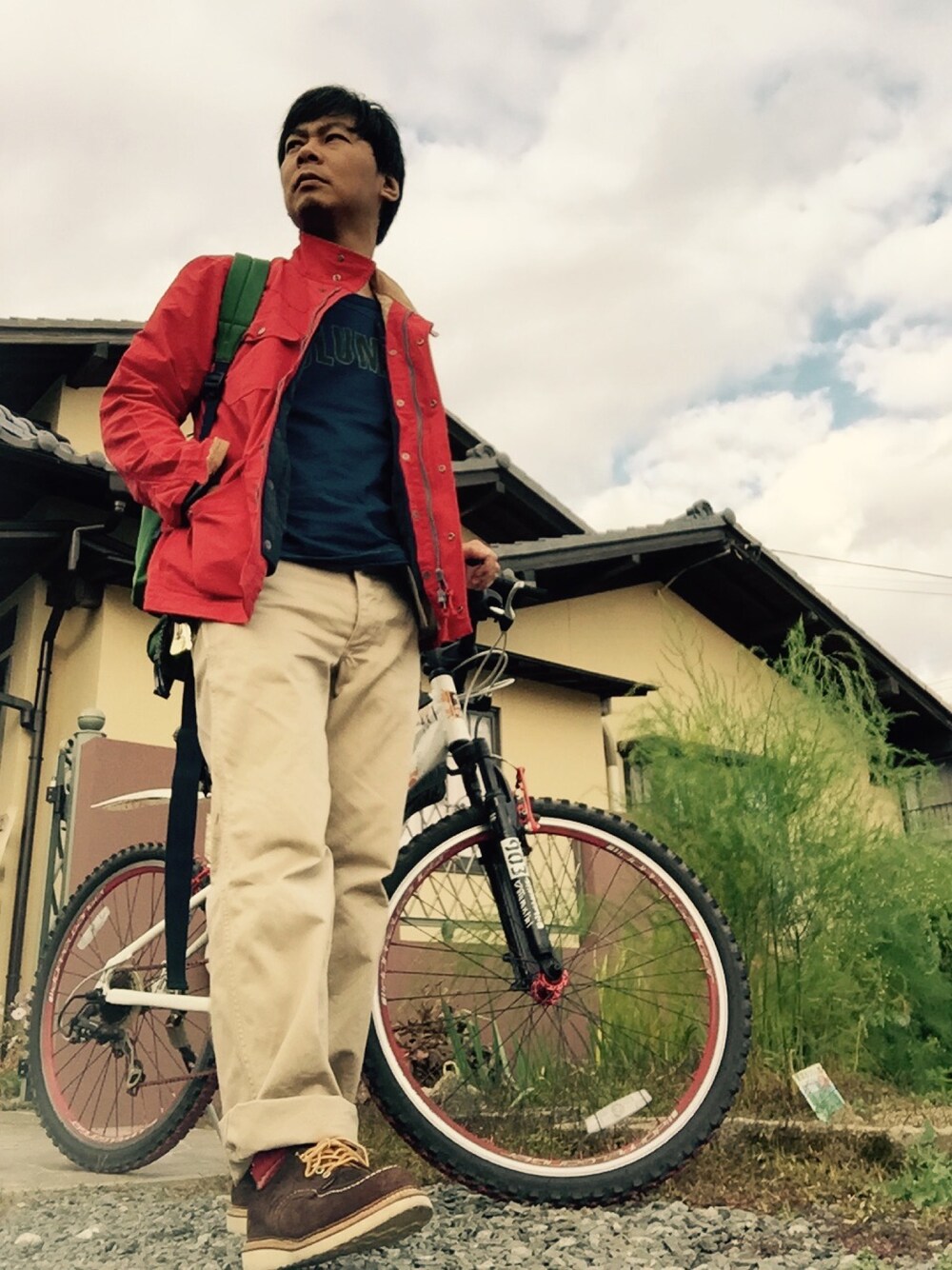 レッド系のブルゾン、ブルー系のTシャツ/カットソー、ベージュ系のチノパンツを着用したメンズの秋コーディネートの1枚目の写真