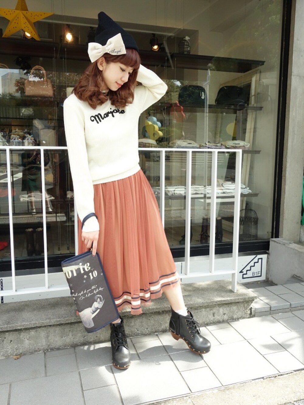 ホワイト系のニット/セーター、グレー系のクラッチバッグ、オレンジ系のスカートを着用したレディースの秋コーディネートの1枚目の写真