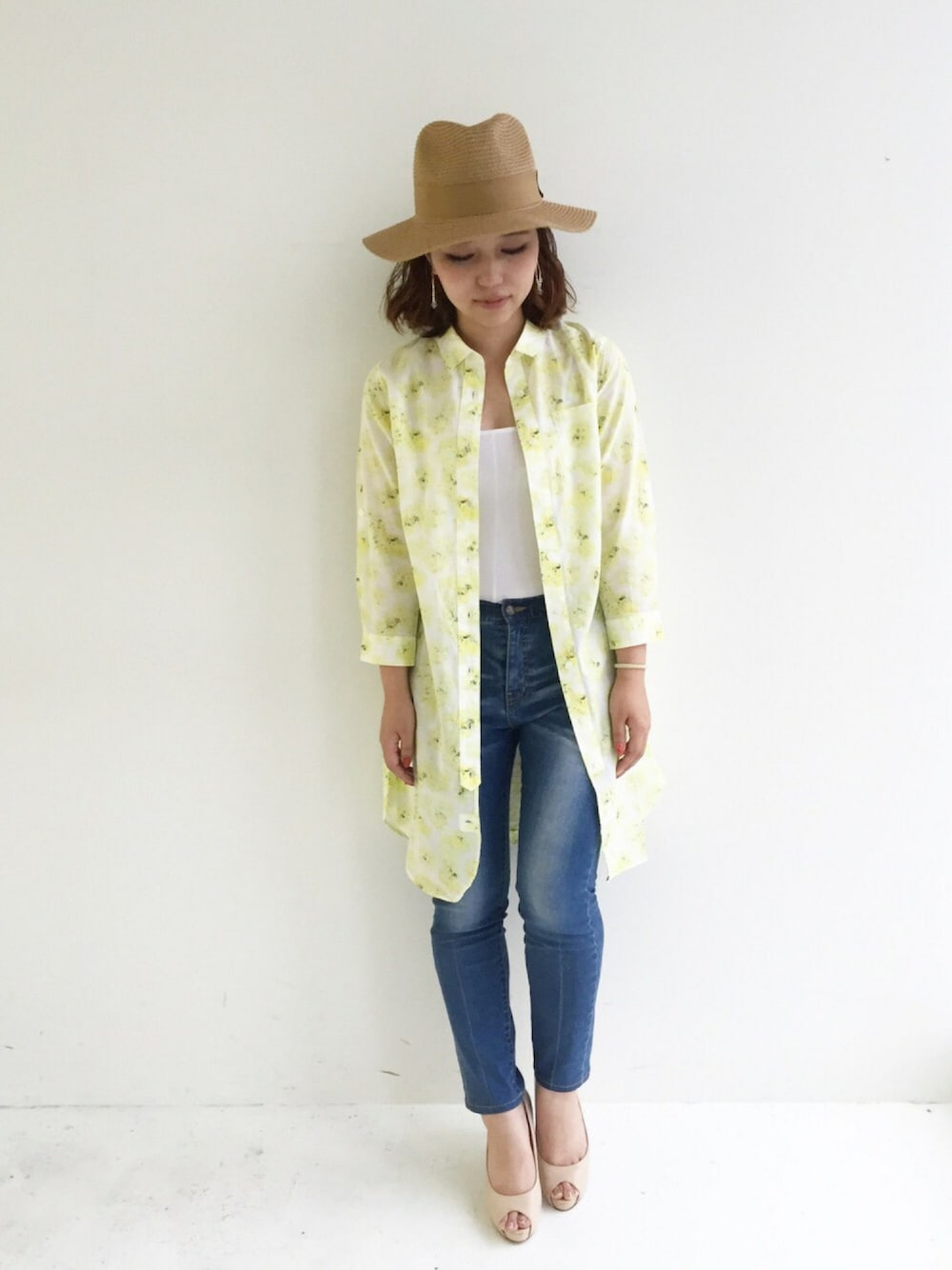 イエロー系のシャツワンピース、ブルー系のデニムパンツ、ベージュ系のパンプスを着用したレディースの夏コーディネートの1枚目の写真