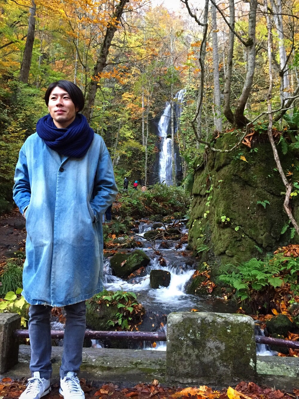 ブルー系のステンカラーコート、グレー系のデニムパンツ、グレー系のスニーカーを着用したメンズの秋コーディネートの1枚目の写真