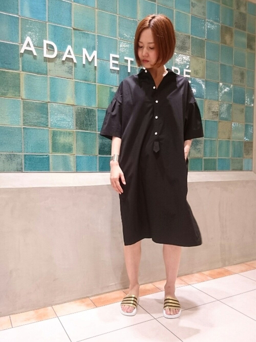 ブラック系のシャツワンピース、ゴールド系のサンダル、シルバー系のバングル/リストバンドを着用したレディースの春コーディネートの1枚目の写真