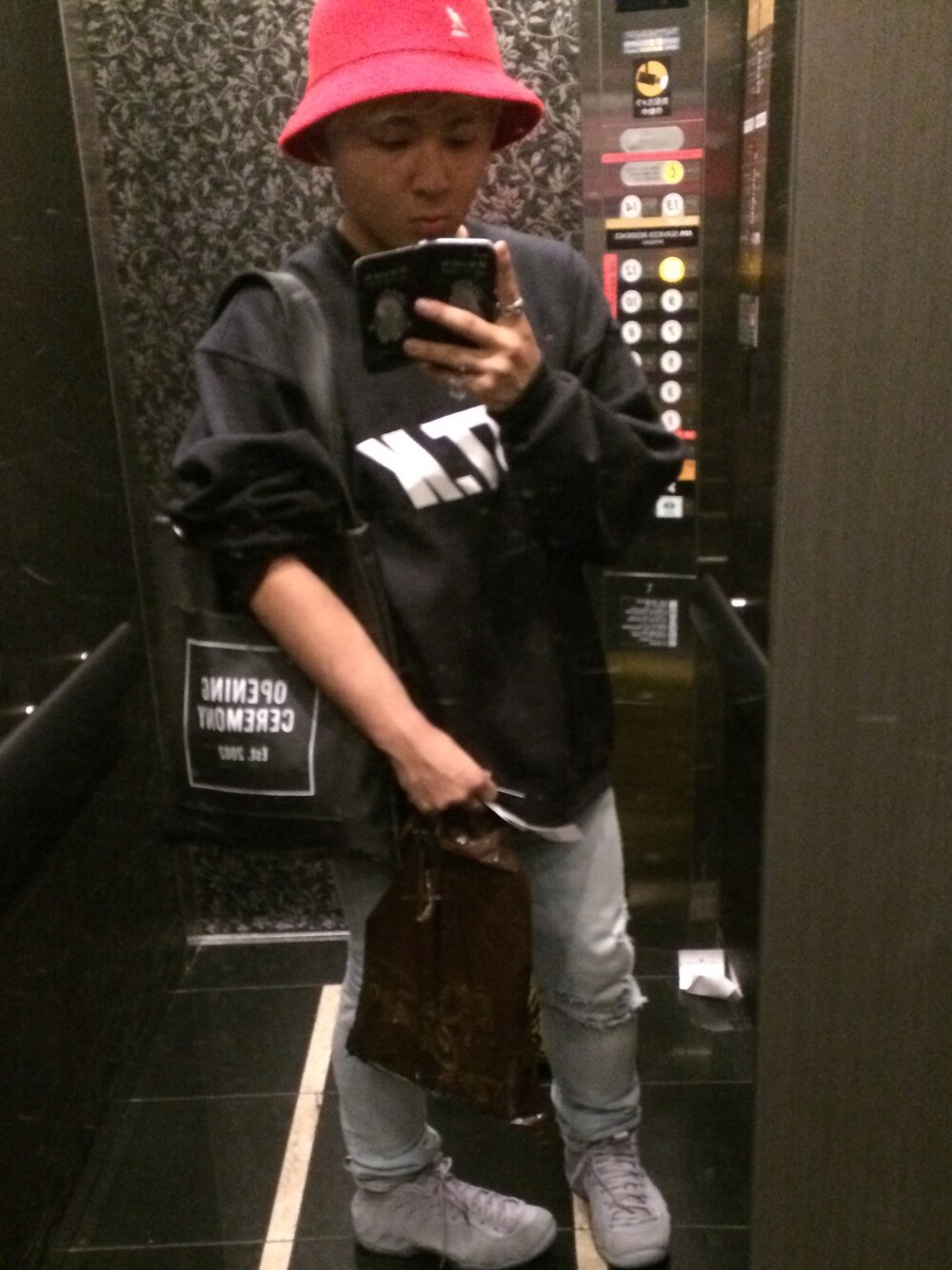 ブラック系のトートバッグ、ブラック系のスウェット、レッド系のハットを着用したメンズの秋コーディネートの1枚目の写真