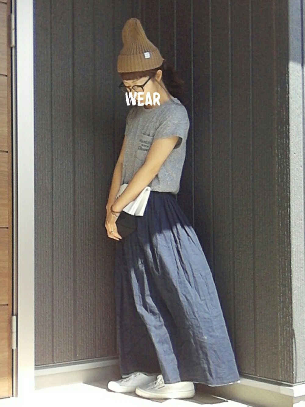 ブラック系のクラッチバッグ、ホワイト系のスニーカー、グレー系のTシャツ/カットソーを着用したレディースの夏コーディネートの1枚目の写真