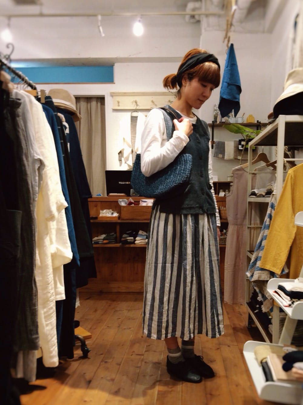 グリーン系のかごバッグ、ホワイト系のスカート、ブルー系のベストを着用したレディースの春コーディネートの1枚目の写真