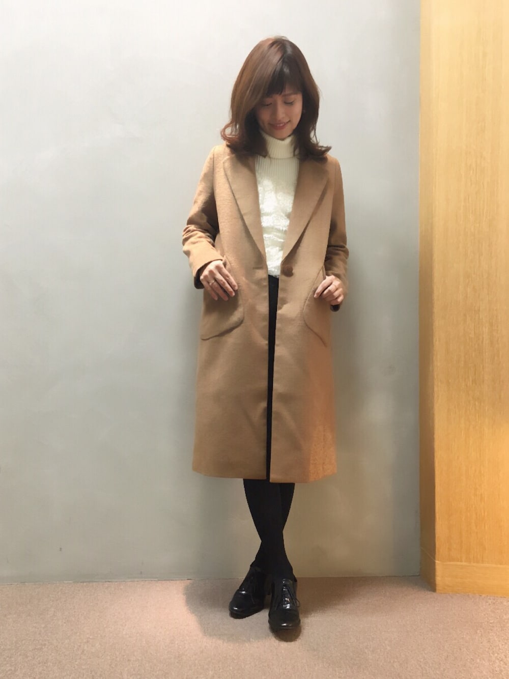 イエロー系のチェスターコート、ブラック系のドレスシューズ、ベージュ系のニット/セーターを着用したレディースの秋コーディネートの1枚目の写真