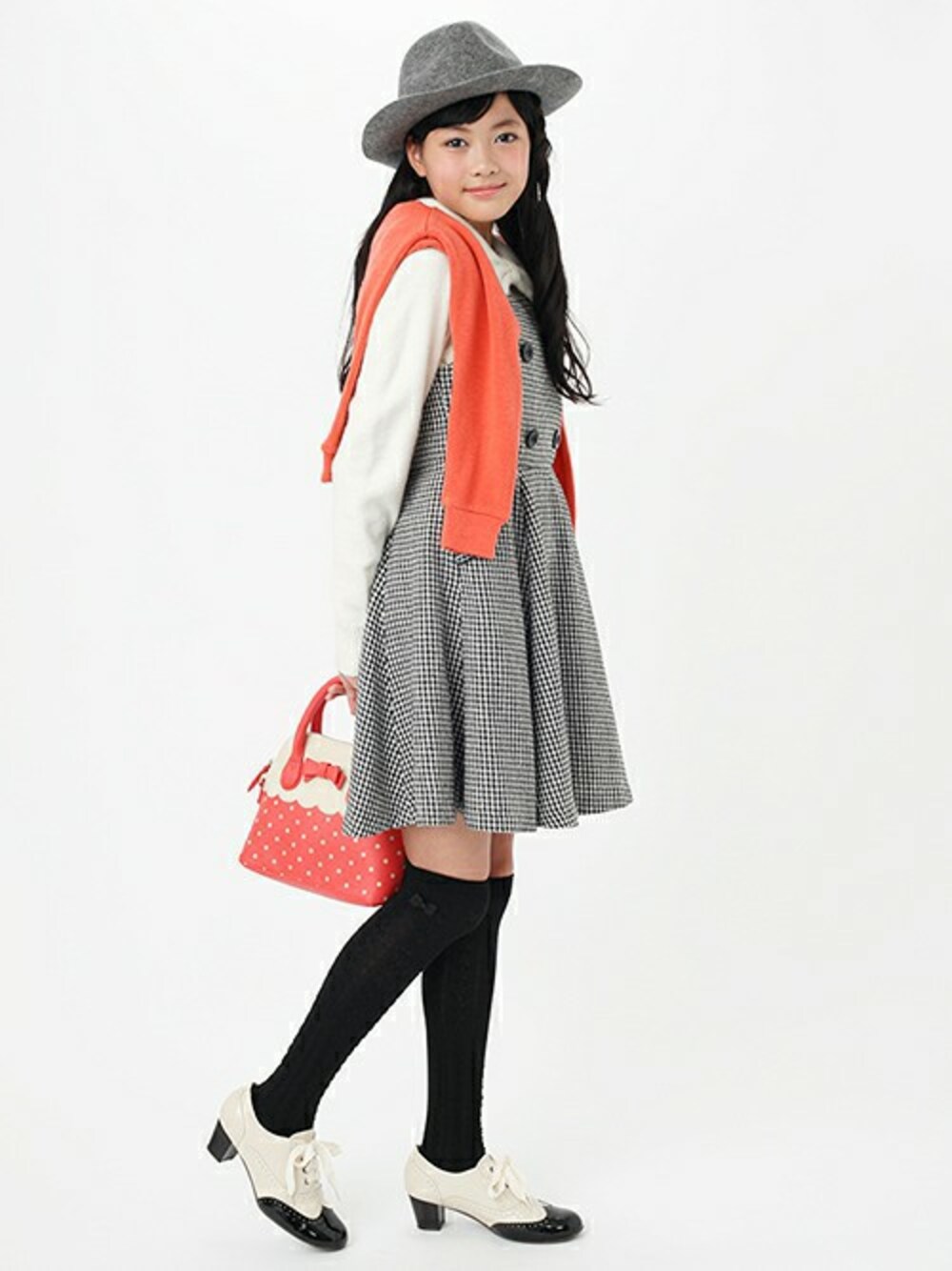 ブラック系のジャンパースカート、ピンク系のカーディガン/ボレロ、ホワイト系のブーティを着用したキッズの冬コーディネートの1枚目の写真