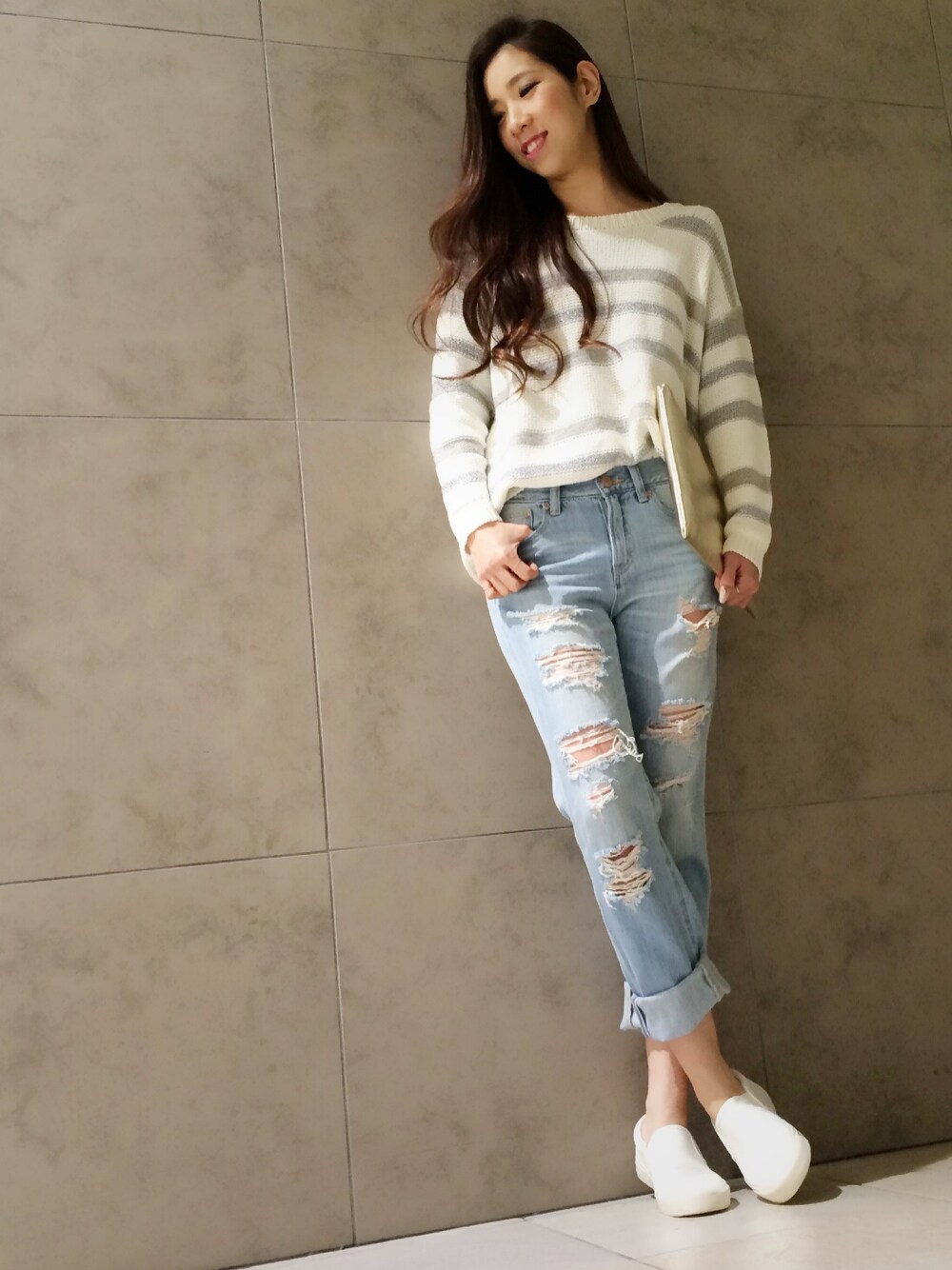 ホワイト系のニット/セーター、ブルー系のデニムパンツ、ゴールド系のクラッチバッグを着用したレディースの冬コーディネートの1枚目の写真