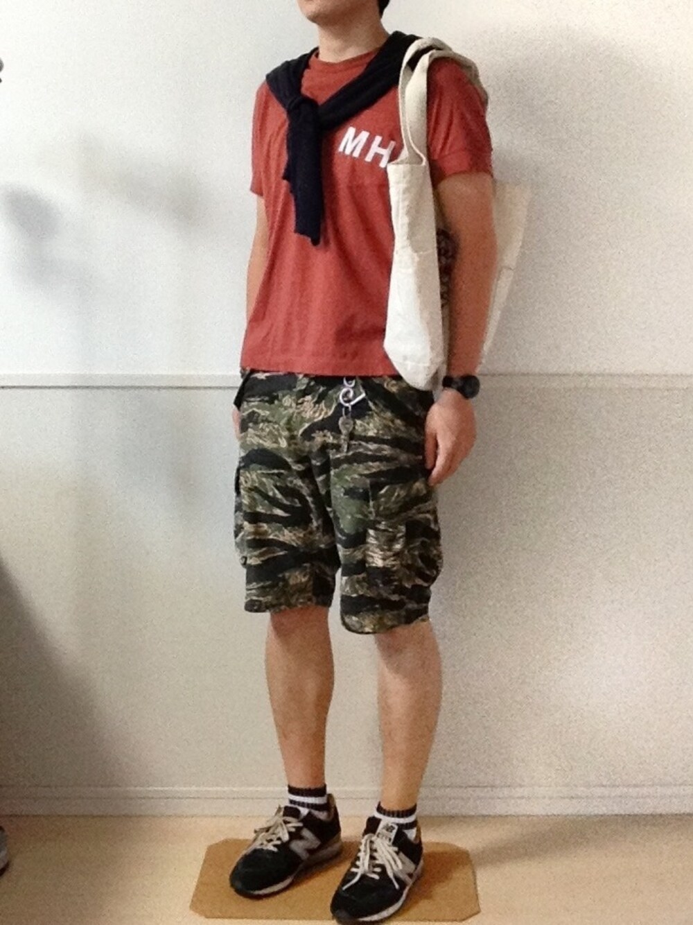 オレンジ系のTシャツ/カットソー、ブラック系のスニーカー、グリーン系のカーゴパンツを着用したメンズの夏コーディネートの1枚目の写真