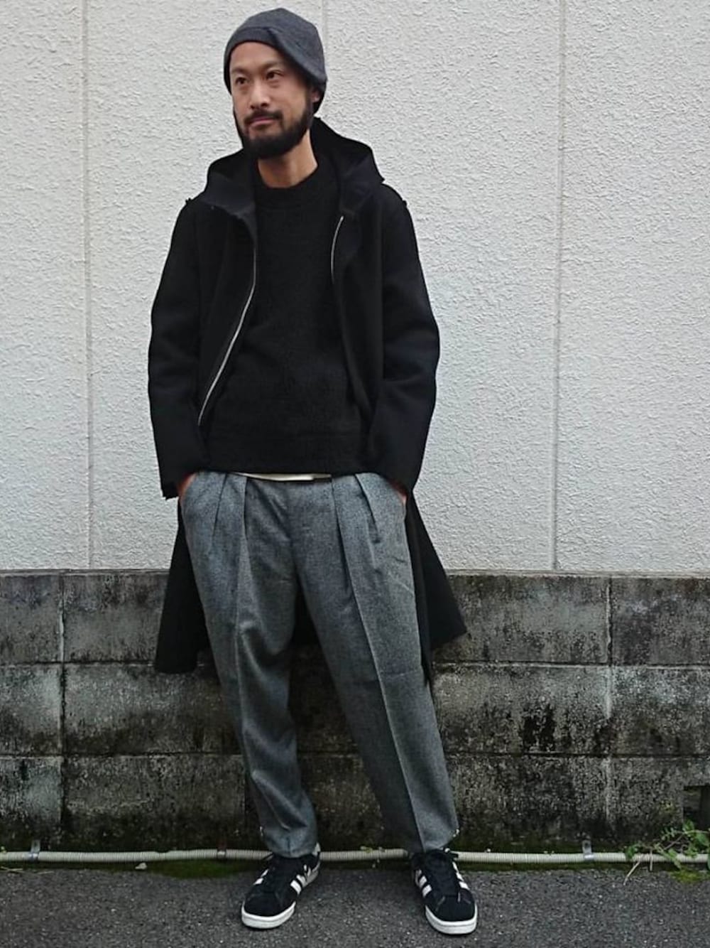 ブラック系のステンカラーコート、ブラック系のニット/セーター、グレー系のスラックスを着用したメンズの秋コーディネートの1枚目の写真