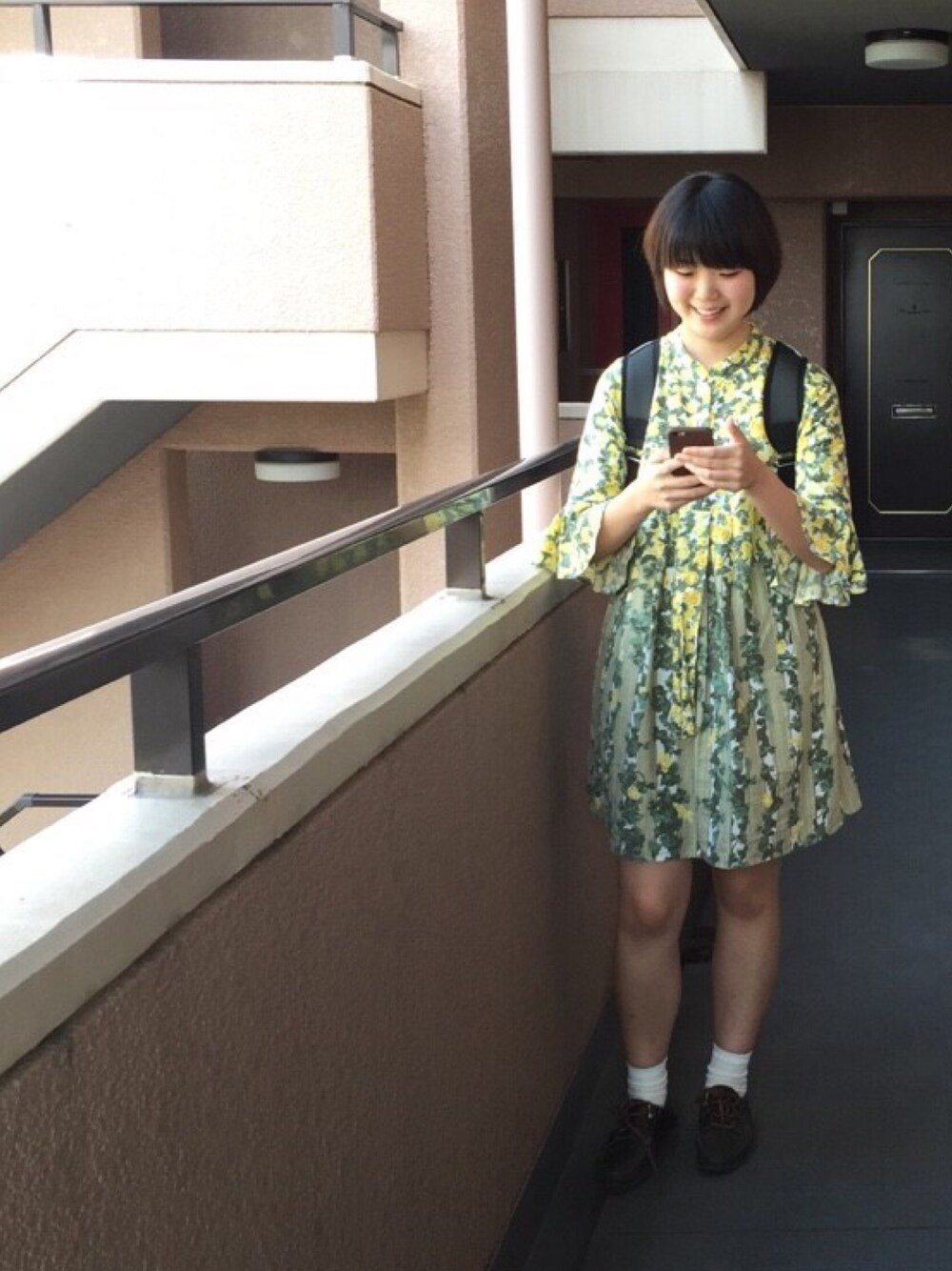 イエロー系のワンピース、グリーン系のモカシン/デッキシューズ、グレー系のバックパック/リュックを着用したレディースの秋コーディネートの1枚目の写真