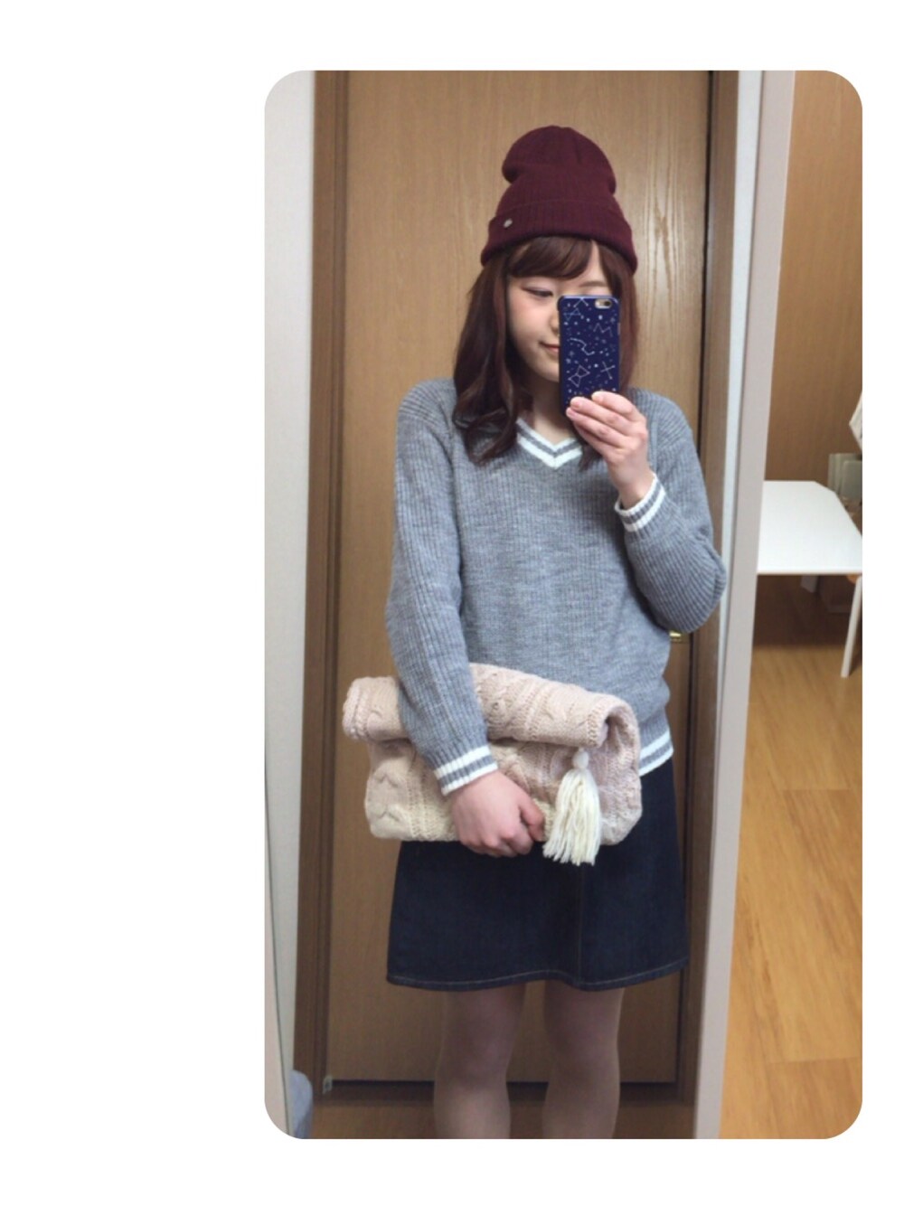 グレー系のニット/セーター、ベージュ系のクラッチバッグ、ブルー系のデニムスカートを着用したレディースの秋コーディネートの1枚目の写真