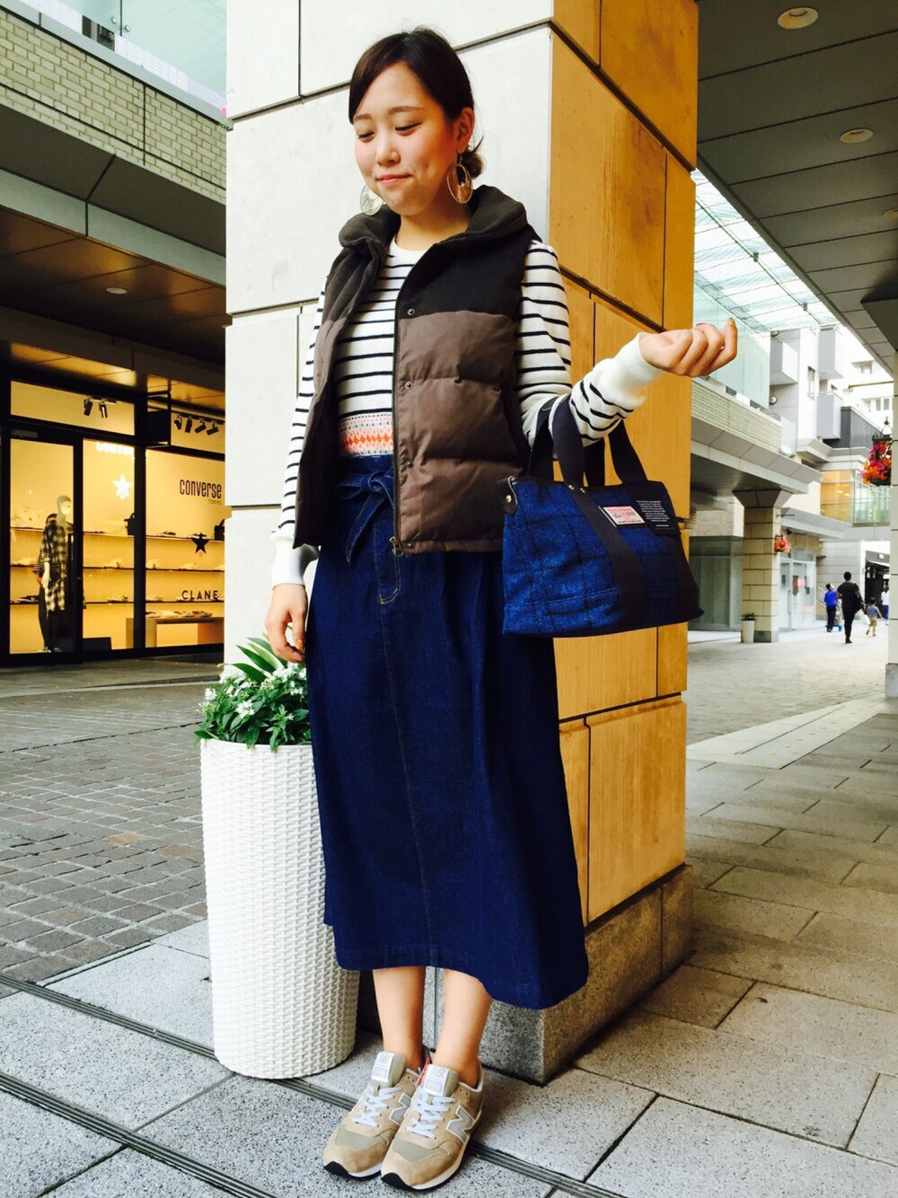 ブラウン系のダウンベスト、ブルー系のスカートを着用したレディースの秋コーディネートの1枚目の写真