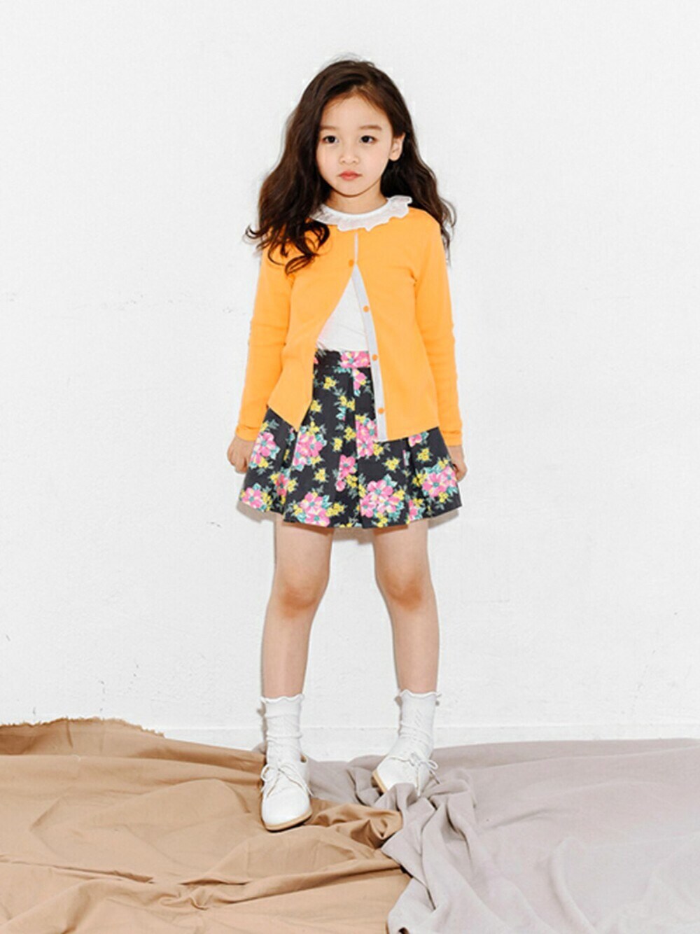 ブラック系のスカート、オレンジ系のカーディガン/ボレロ、ホワイト系のその他トップスを着用したキッズの冬コーディネートの1枚目の写真