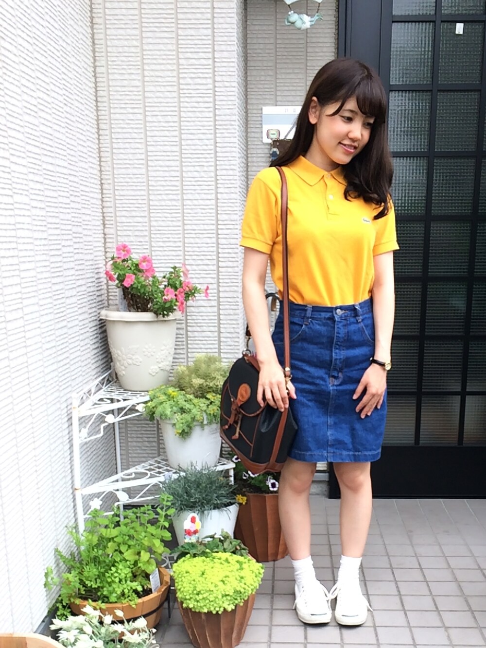 イエロー系のポロシャツ、ブルー系のデニムスカート、ブラック系のショルダーバッグを着用したレディースの夏コーディネートの1枚目の写真