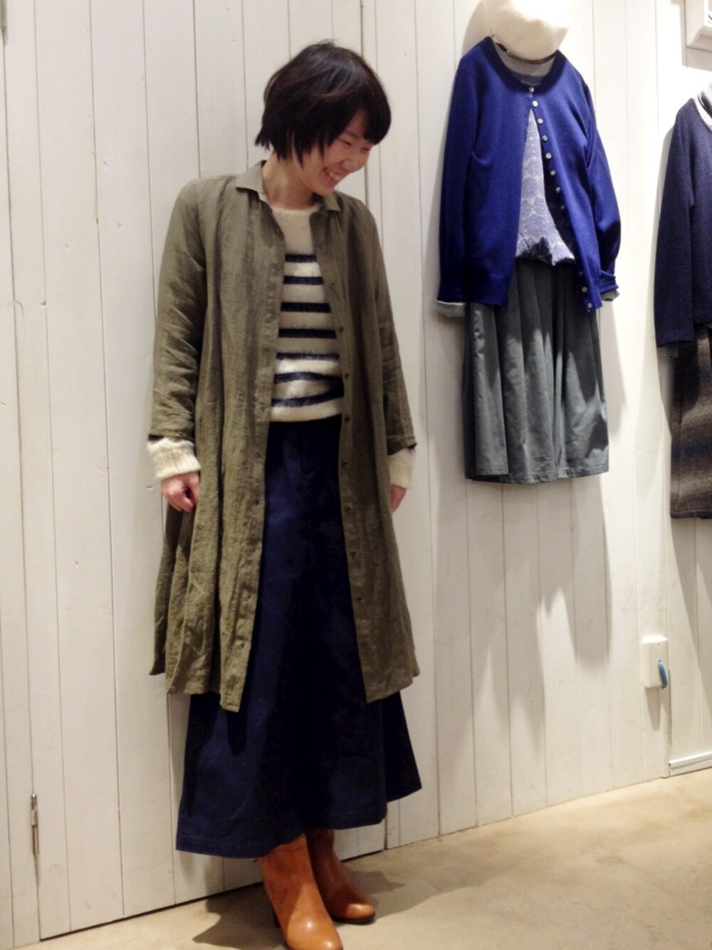 ホワイト系のニット/セーター、グリーン系のシャツワンピース、ブルー系のスカートを着用したレディースの冬コーディネートの1枚目の写真