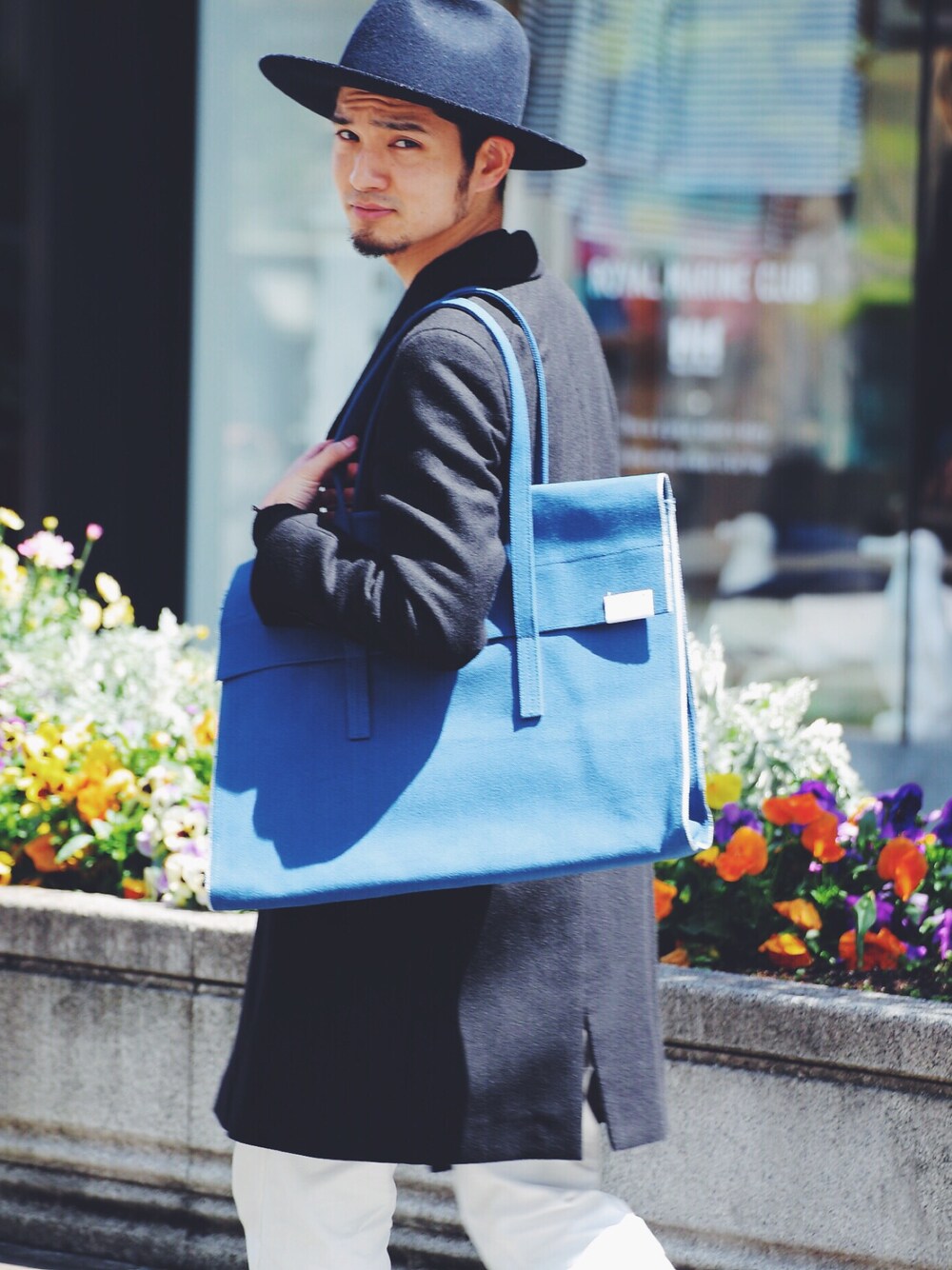ブルー系のトートバッグ、ブラック系のチェスターコート、ホワイト系のカーゴパンツを着用したメンズの春コーディネートの1枚目の写真