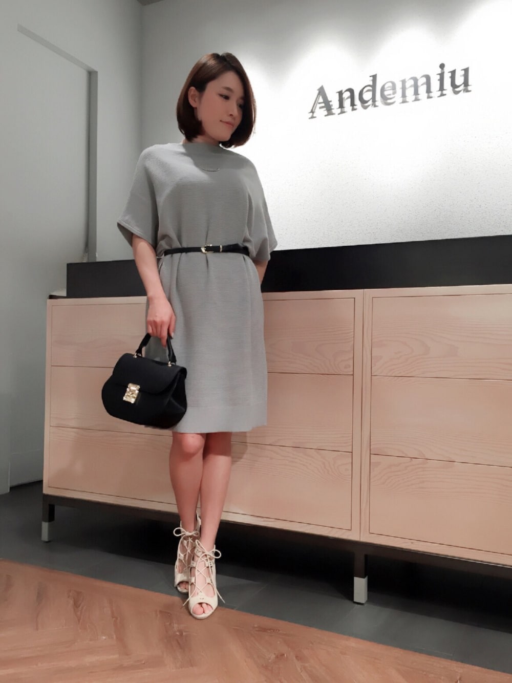 グレー系のワンピース、ベージュ系のサンダル、ブラック系のショルダーバッグを着用したレディースの春コーディネートの1枚目の写真
