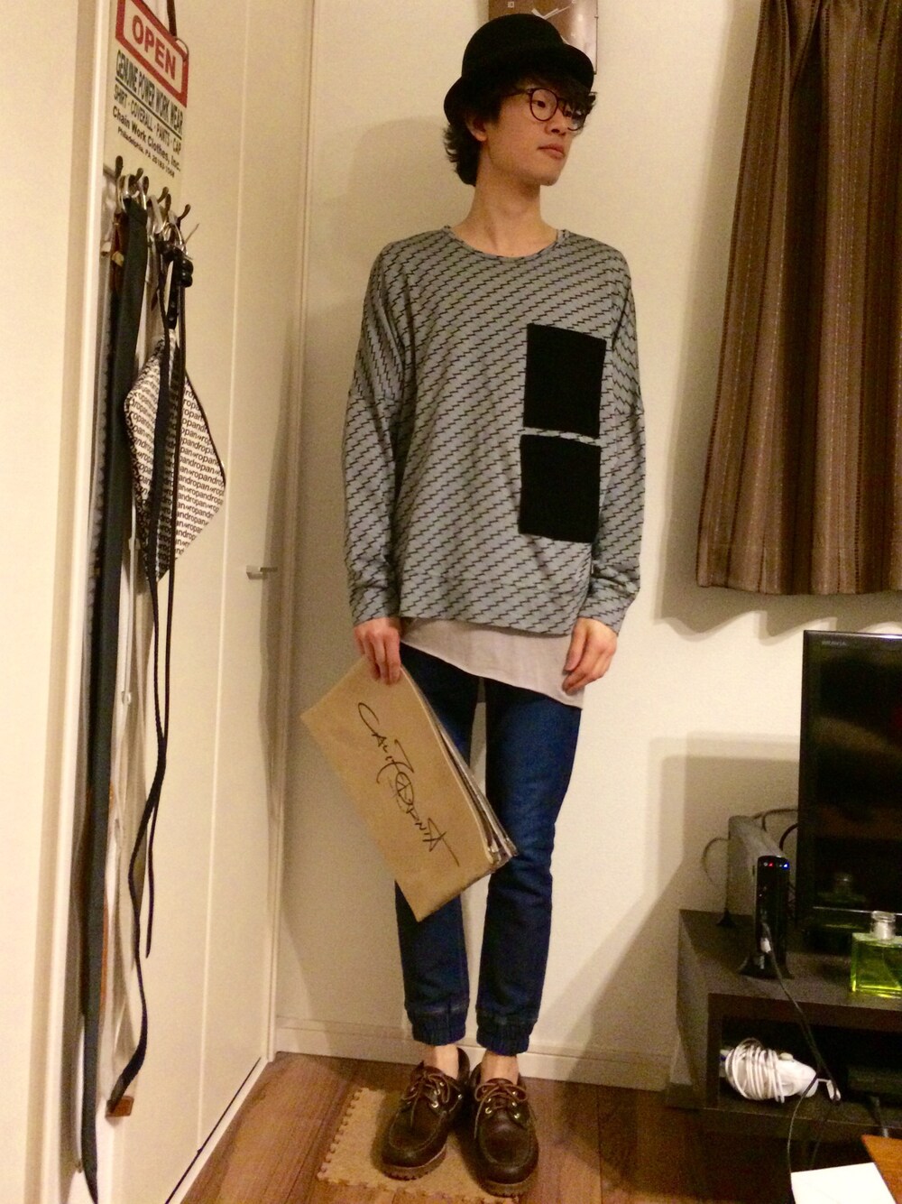 グレー系のトップス、ブルー系のデニムパンツ、ベージュ系のクラッチバッグを着用したメンズの春コーディネートの1枚目の写真