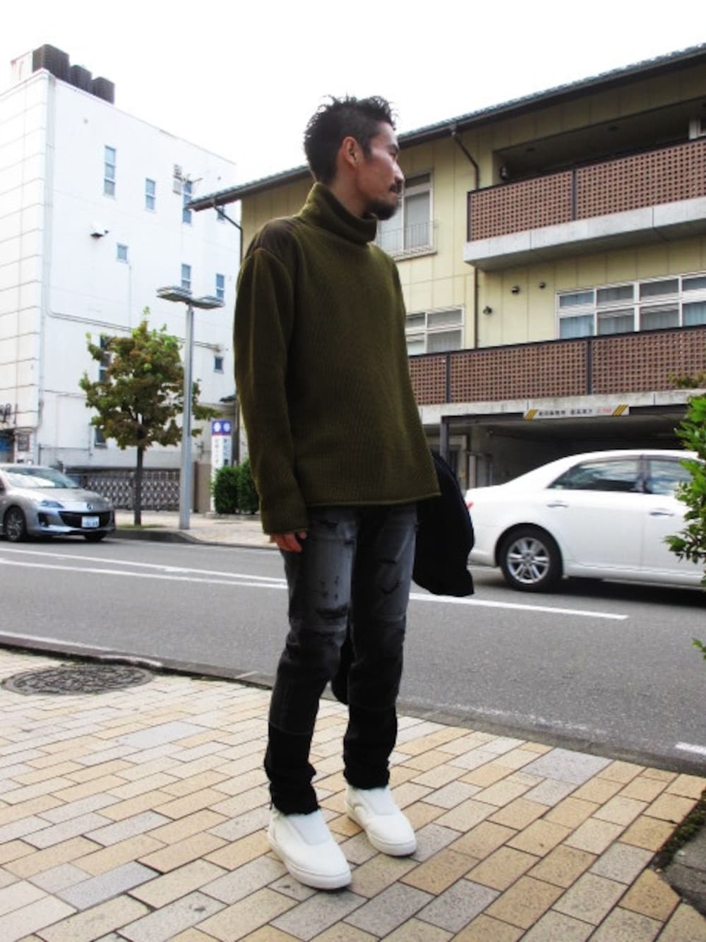 グリーン系のニット/セーター、ホワイト系のスニーカー、ブラック系のデニムパンツを着用したメンズの秋コーディネートの1枚目の写真
