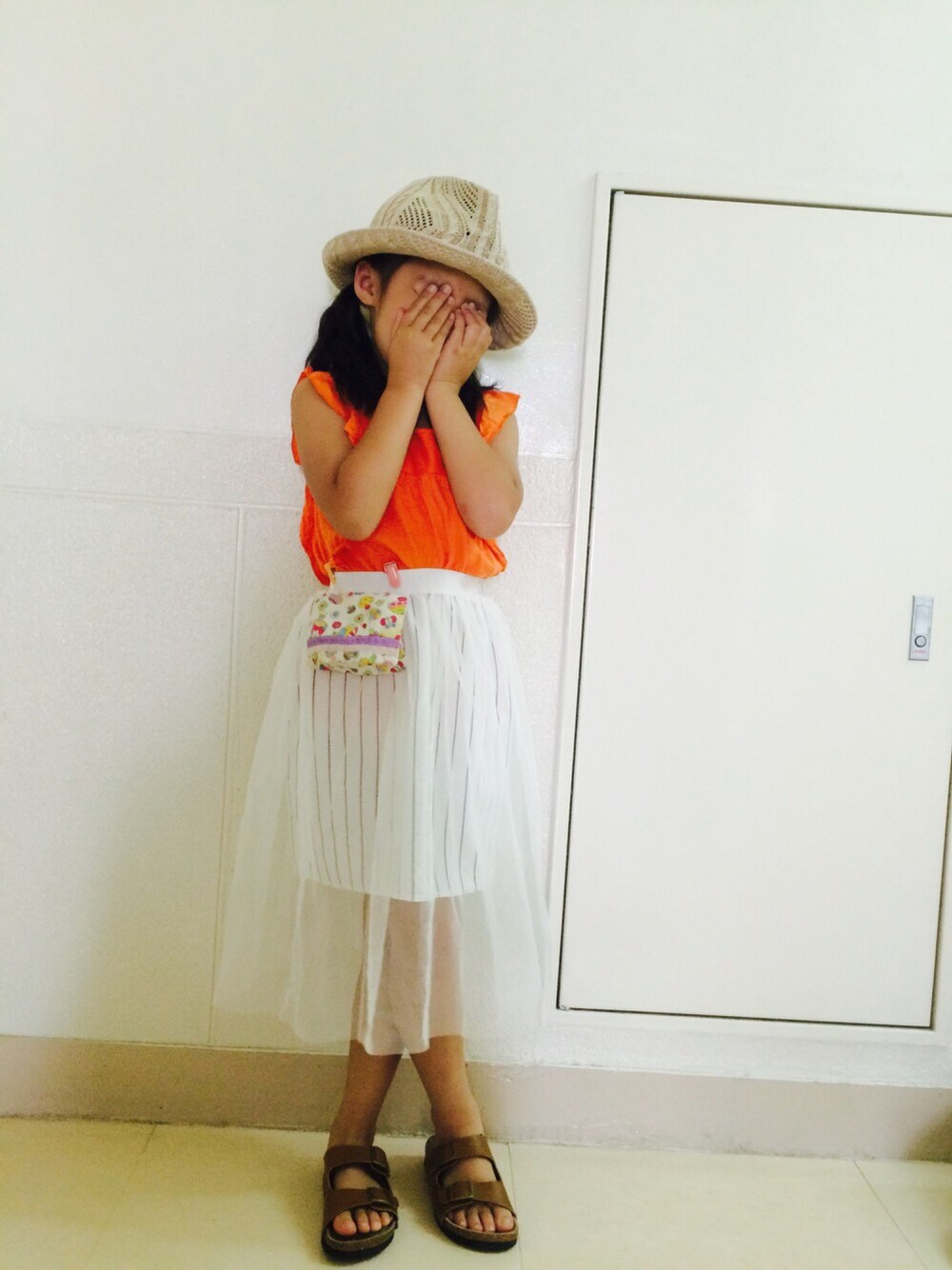 オレンジ系のTシャツ/カットソー、ホワイト系のスカート、ブラウン系のサンダルを着用したキッズの春コーディネートの1枚目の写真