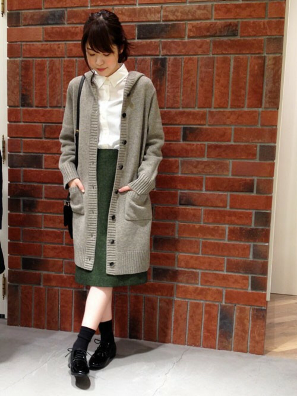 グレー系のニット/セーター、グリーン系のスカート、ホワイト系のシャツ/ブラウスを着用したレディースの秋コーディネートの1枚目の写真