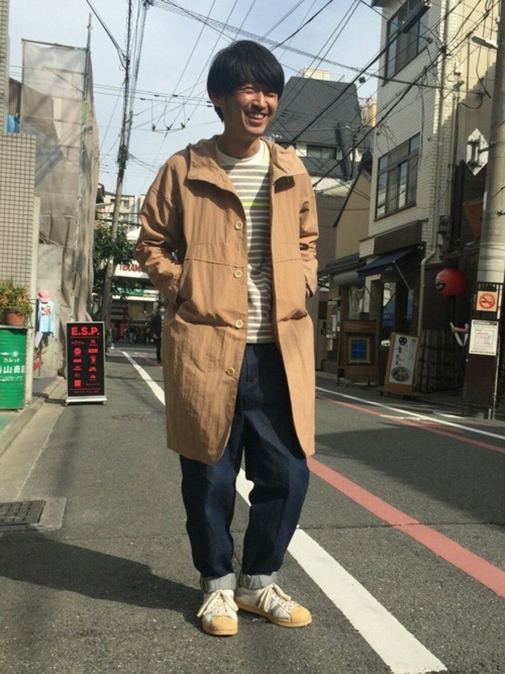 ベージュ系のステンカラーコート、グレー系のTシャツ/カットソー、ブルー系のデニムパンツを着用したメンズの春コーディネートの1枚目の写真