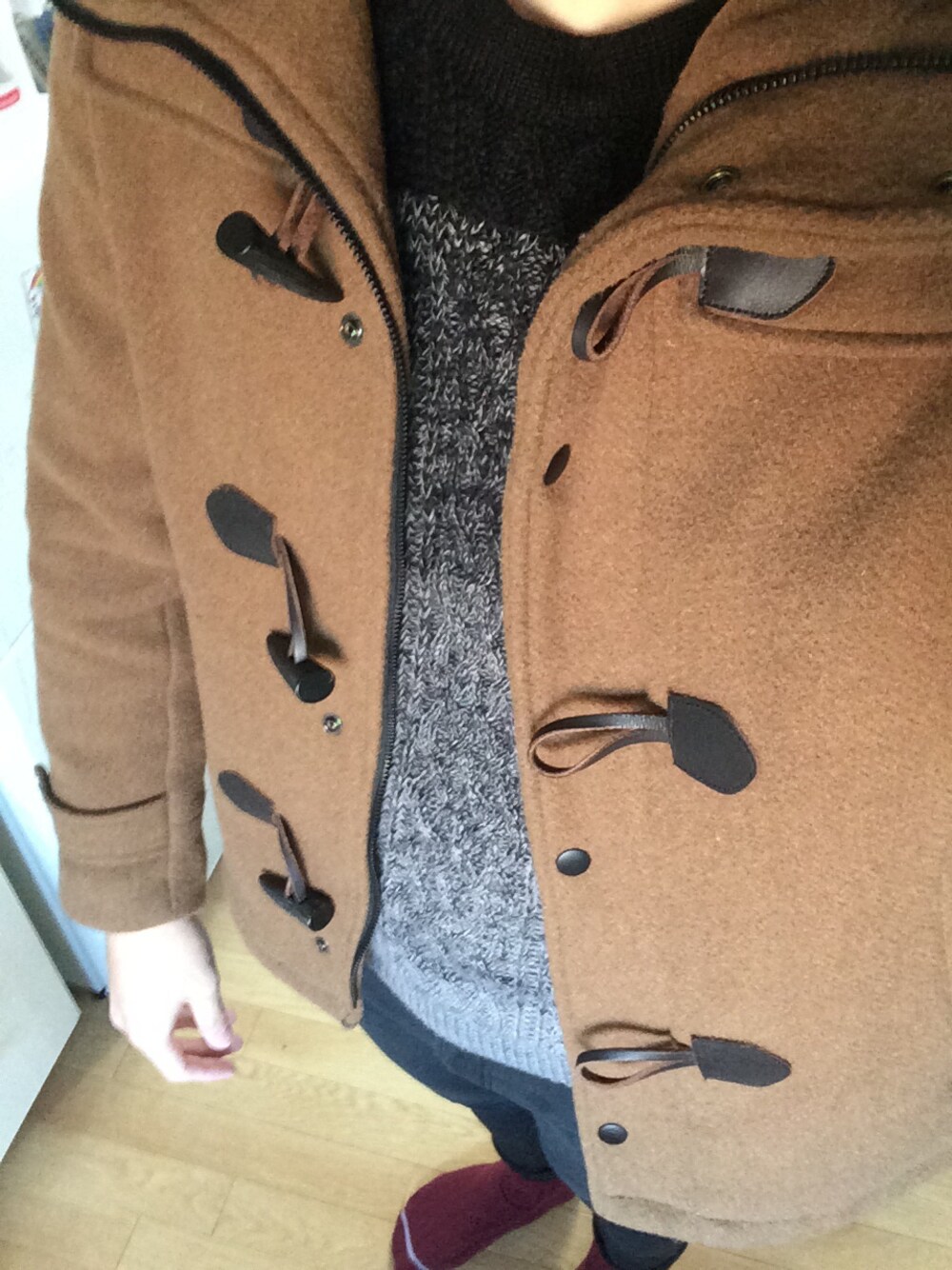 イエロー系のダッフルコート、ブラック系のニット/セーター、ブラック系のスニーカーを着用したメンズの冬コーディネートの1枚目の写真