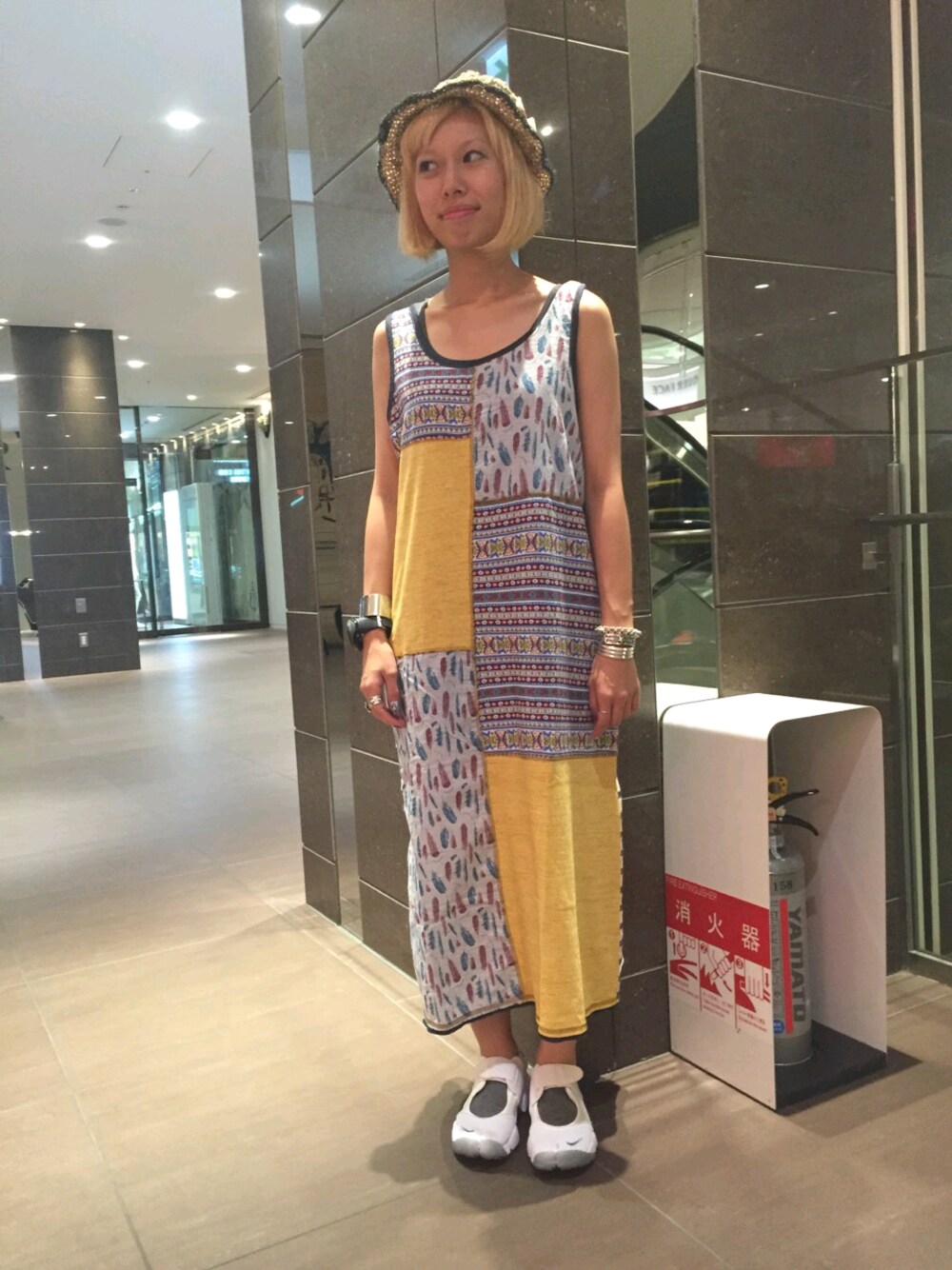 イエロー系のワンピース、ベージュ系のハットを着用したレディースの夏コーディネートの1枚目の写真